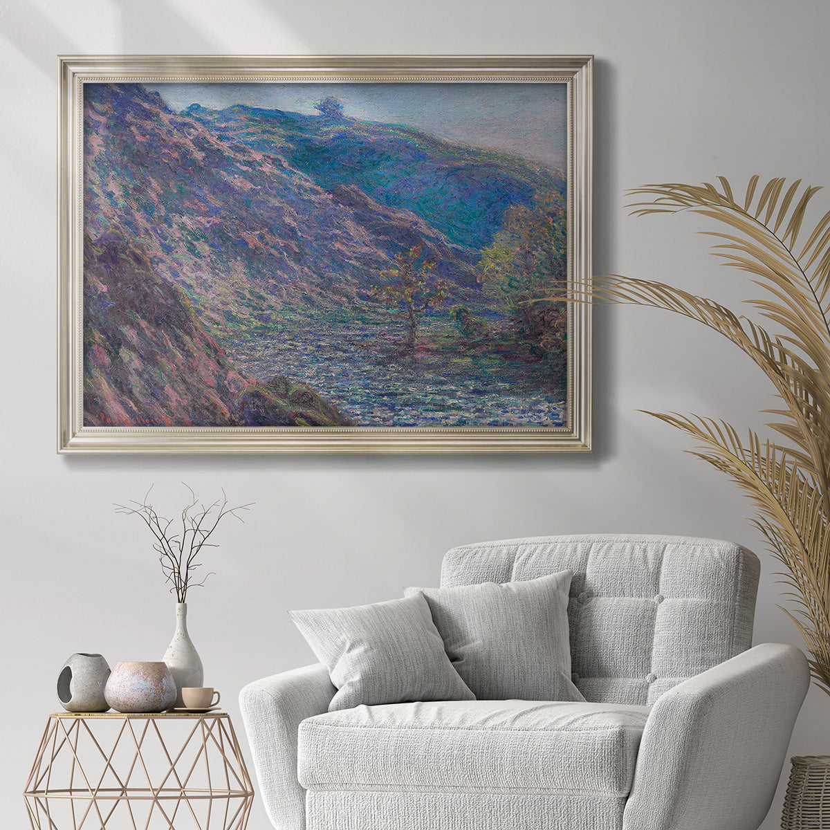 Impressionist river valley landscape by Claude Monet in an ornate champagne frame displayed in a bright interior setting.