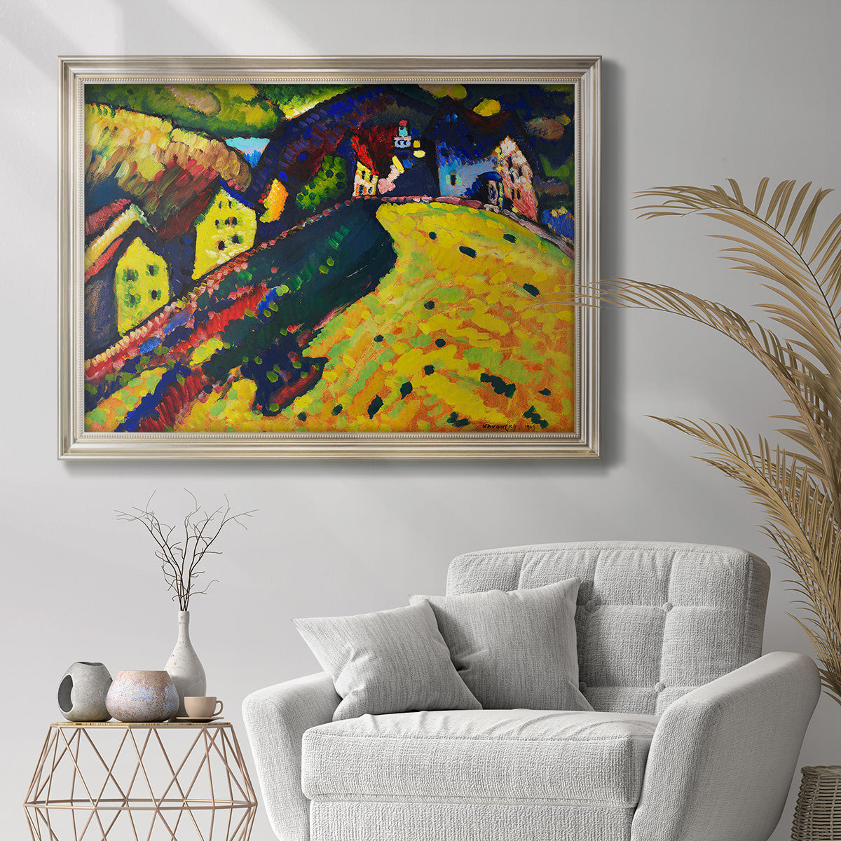 Expressionist village landscape by Wassily Kandinsky in an ornate champagne frame displayed in a bright interior setting.