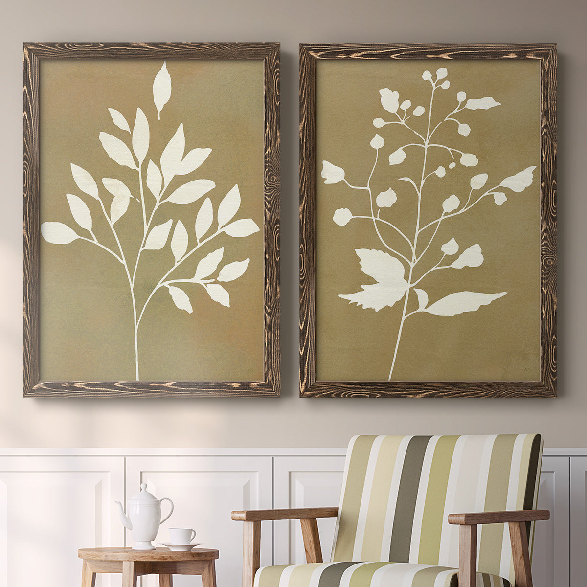 Set of two walnut barnwood framed canvas prints depicting two minimalist botanical silhouettes with white leafy stems against warm honey gold backgrounds above a sideboard in a cozy sitting room.