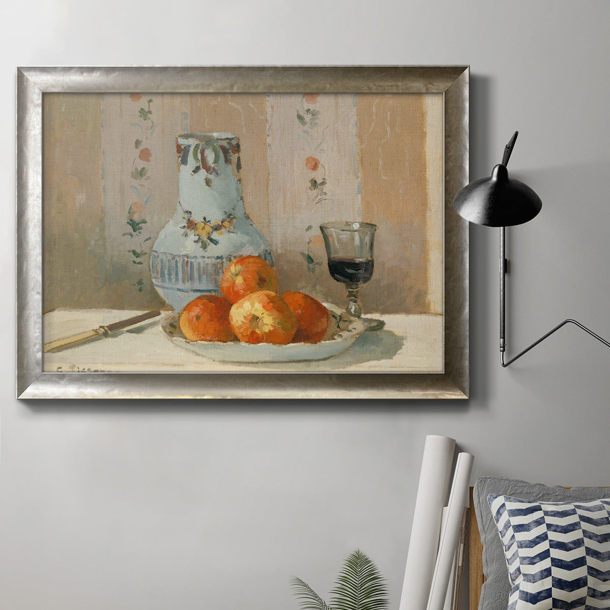 Impressionist still life painting with apples and a ceramic pitcher in an ornate mottled silver frame displayed in a neutral interior setting.