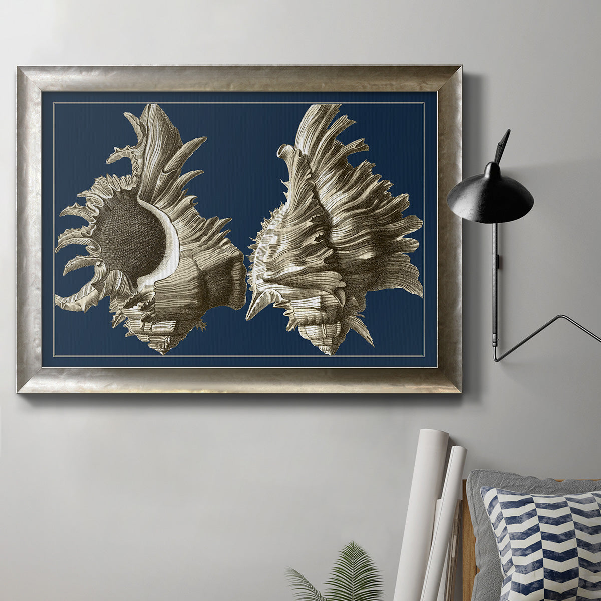 Vintage nautical conch shell artwork on navy background in an ornate mottled silver frame displayed in a neutral interior setting.