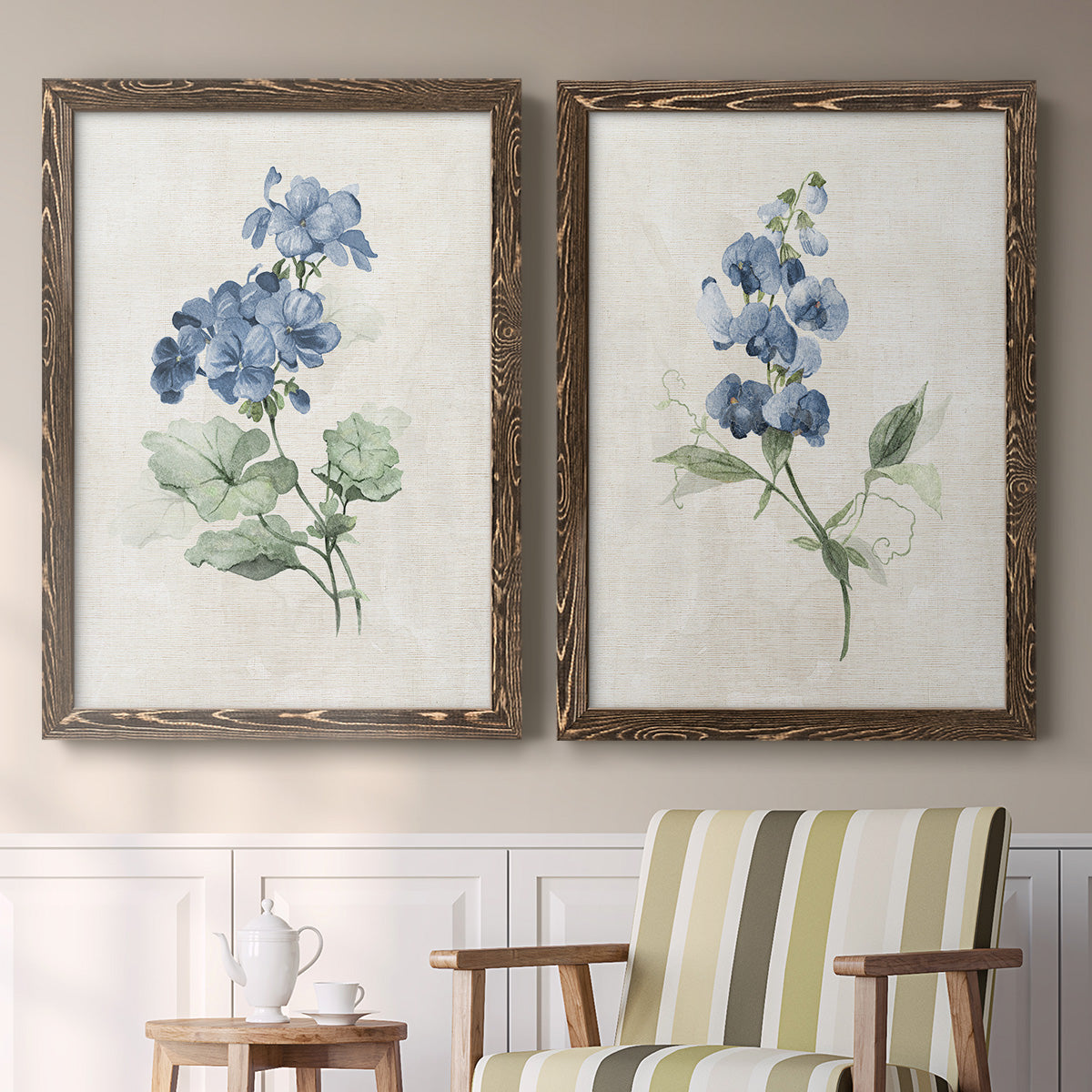 Set of two walnut barnwood framed canvas prints depicting two farmhouse botanical illustrations featuring blue periwinkle flowers with leafy stems above a sideboard in a cozy sitting room.