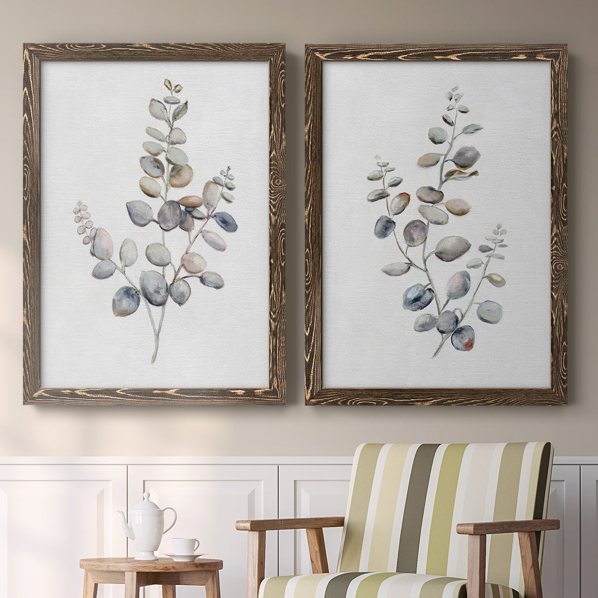 Set of two walnut barnwood framed canvas prints depicting two minimalist watercolor botanical studies featuring delicate eucalyptus branches with rounded leaves above a sideboard in a cozy sitting room.