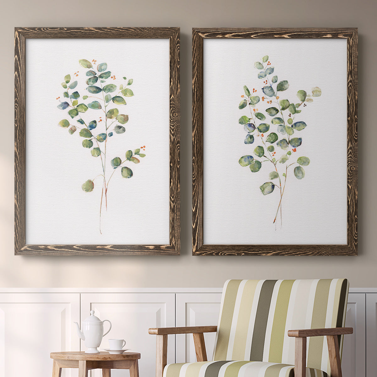 Set of two walnut barnwood framed canvas prints depicting two minimalist watercolor botanical studies featuring delicate eucalyptus branches with rounded leaves above a sideboard in a cozy sitting room.