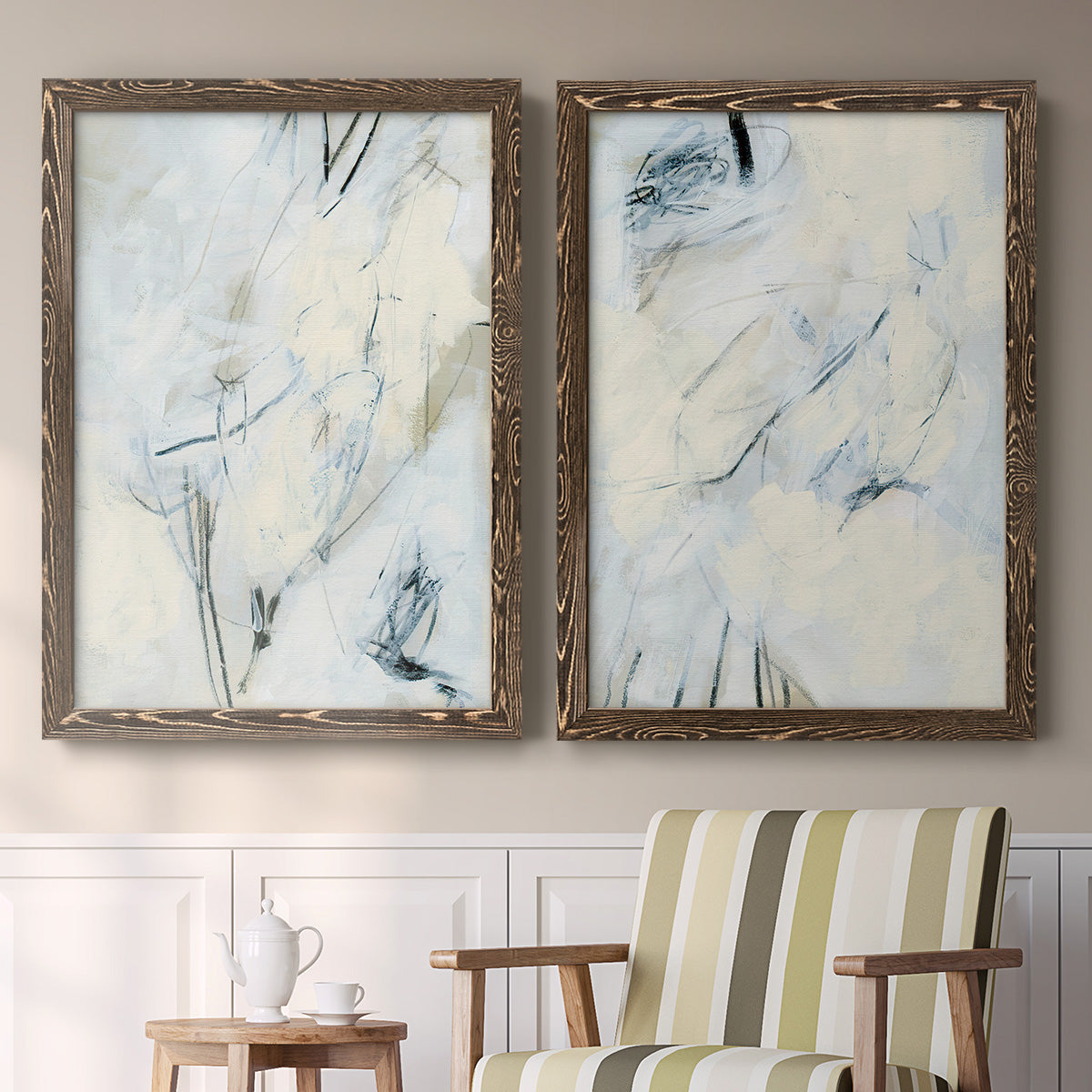 Set of two walnut barnwood framed canvas prints depicting two airy gestural abstracts featuring pale blue cream and charcoal marks drifting across white above a sideboard in a cozy sitting room.