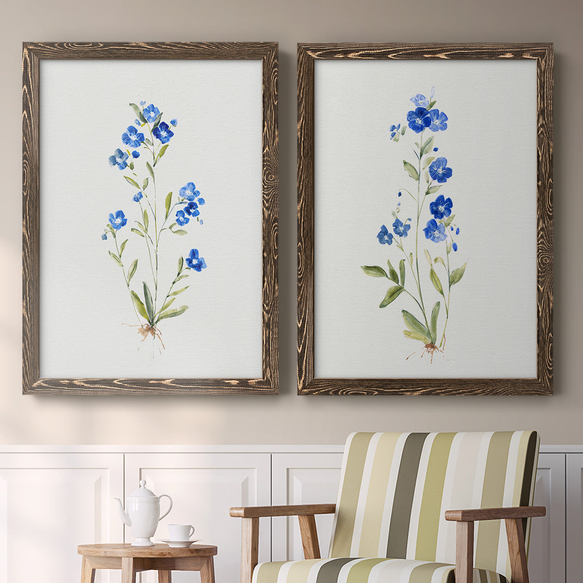 Set of two walnut barnwood framed canvas prints depicting two delicate watercolor botanical studies featuring small blue wildflower stems above a sideboard in a cozy sitting room.