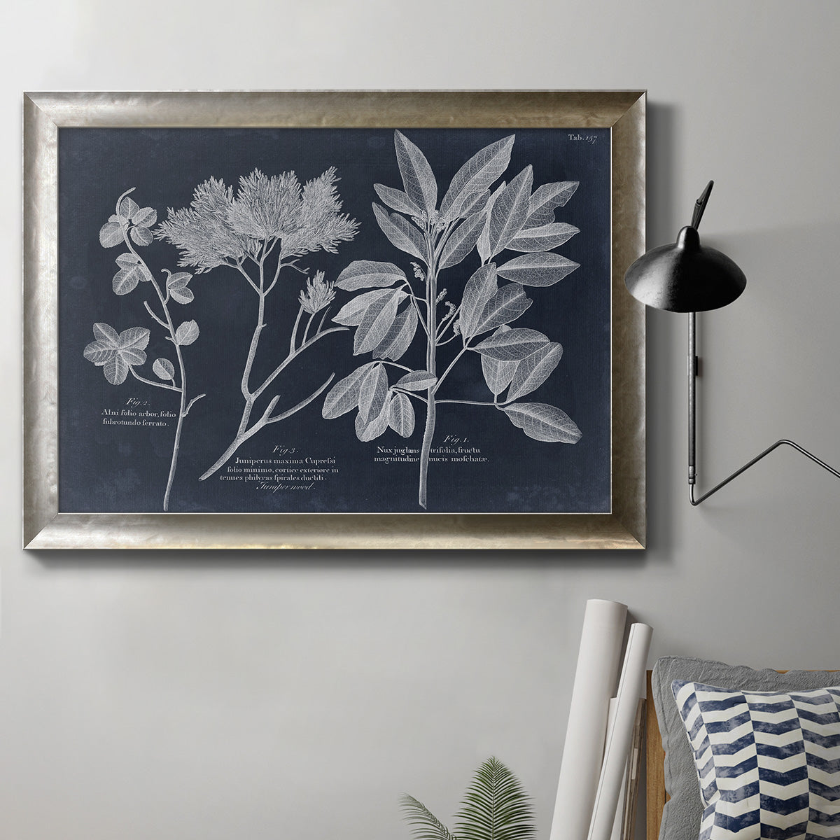 Vintage botanical leaf illustration on dark background in an ornate mottled silver frame displayed in a neutral interior setting.