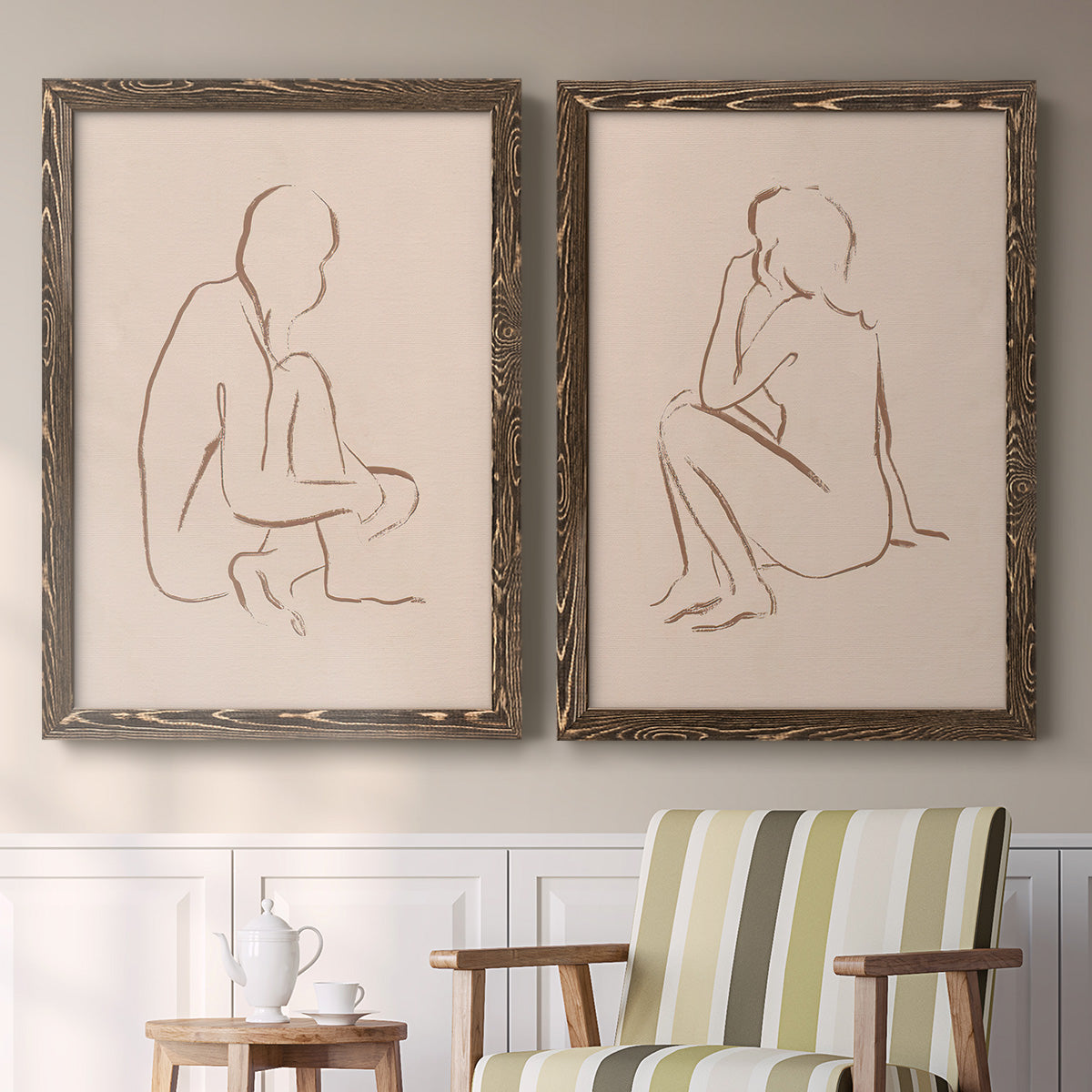 Set of two walnut barnwood framed canvas prints depicting two minimalist figurative sketches featuring seated female figures drawn with single flowing lines above a sideboard in a cozy sitting room.