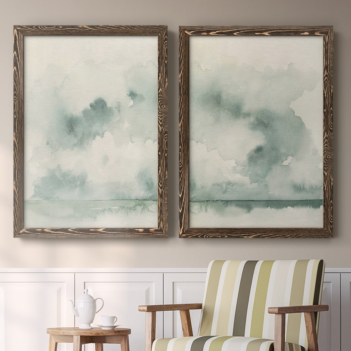 Set of two walnut barnwood framed canvas prints depicting two minimalist watercolor seascapes with misty green clouds calm horizons and pale reflective water above a sideboard in a cozy sitting room.
