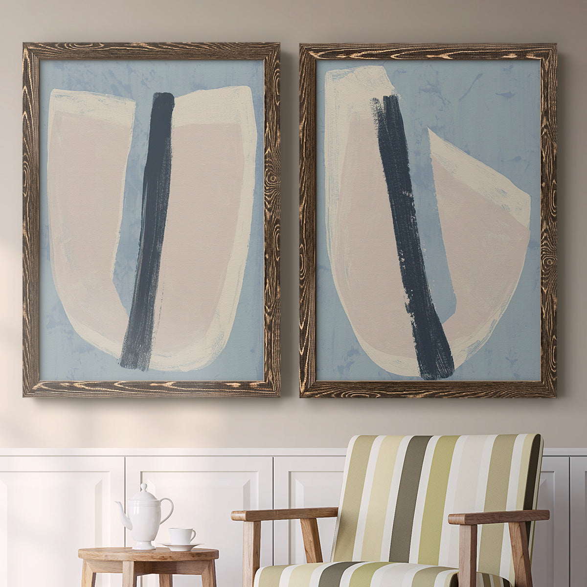 Set of two walnut barnwood framed canvas prints depicting two minimalist collage-style abstracts featuring single navy brush slashes across layered paper-like shapes above a sideboard in a cozy sitting room.