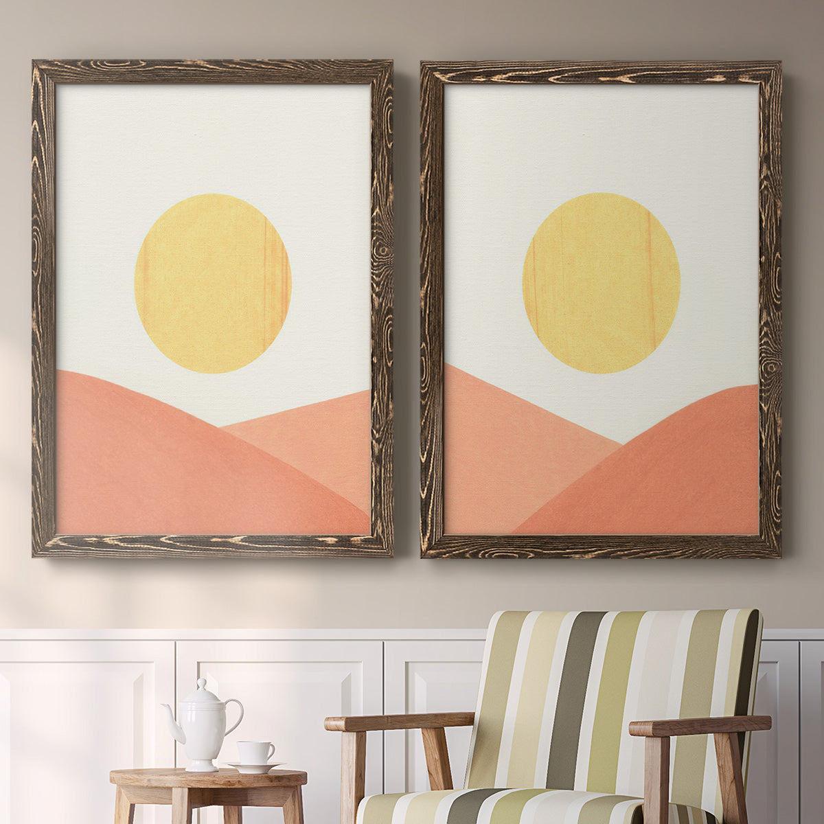 Set of two walnut barnwood framed canvas prints depicting two minimalist boho landscapes featuring yellow suns rising over terracotta geometric hills above a sideboard in a cozy sitting room.