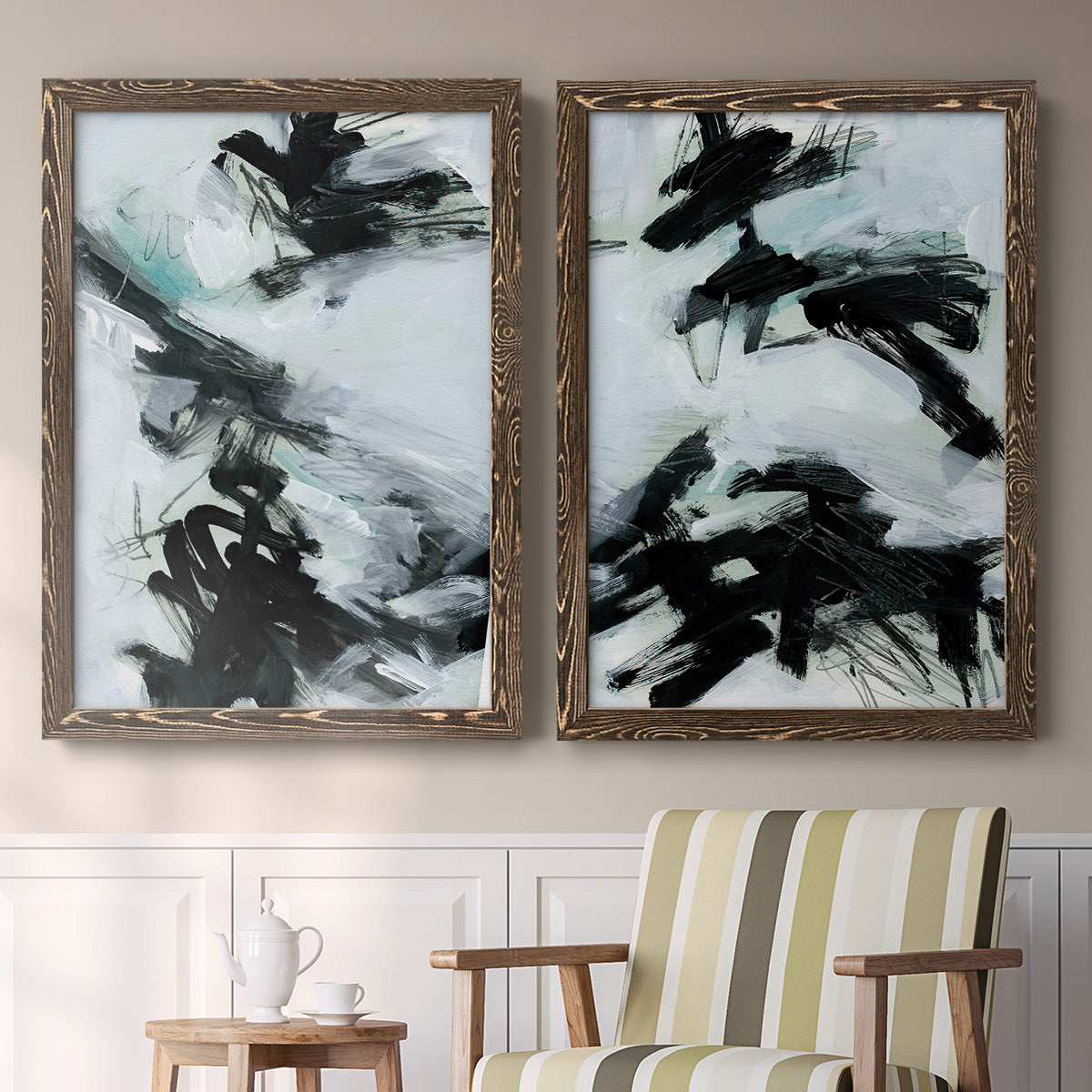 Set of two walnut barnwood framed canvas prints depicting two gestural ocean-inspired abstracts featuring sweeping black brushstrokes over pale blue-gray fields above a sideboard in a cozy sitting room.