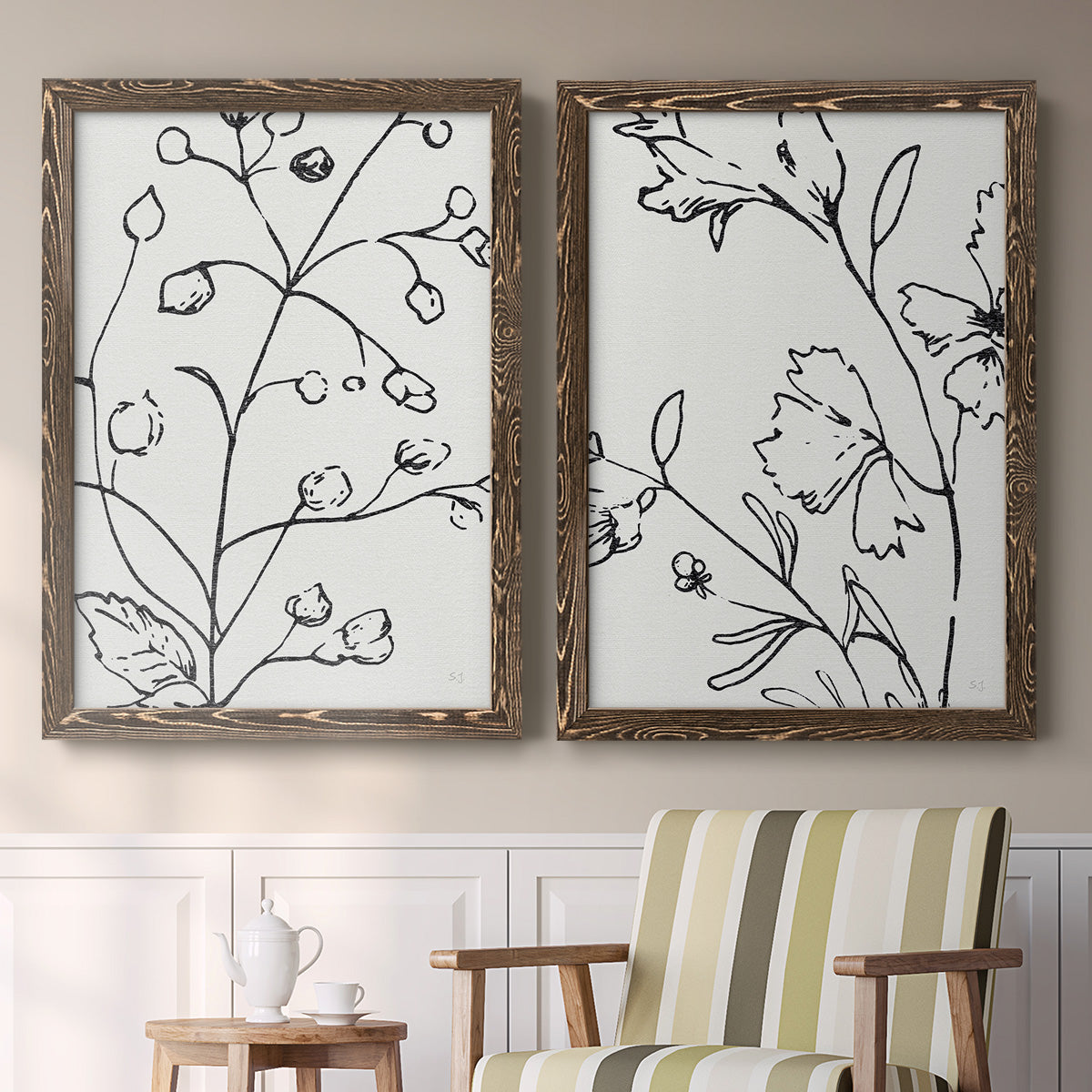 Set of two walnut barnwood framed canvas prints depicting two minimalist botanical line art featuring black contour drawings of leaves and flowers above a sideboard in a cozy sitting room.