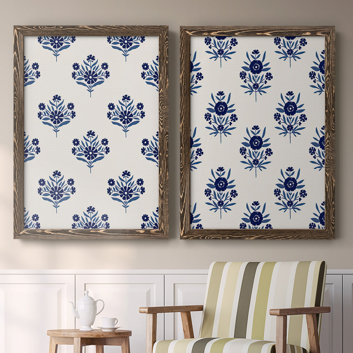 Set of two walnut barnwood framed canvas prints depicting two repeating blue floral patterns with stylized bouquets arranged across warm white backgrounds above a sideboard in a cozy sitting room.
