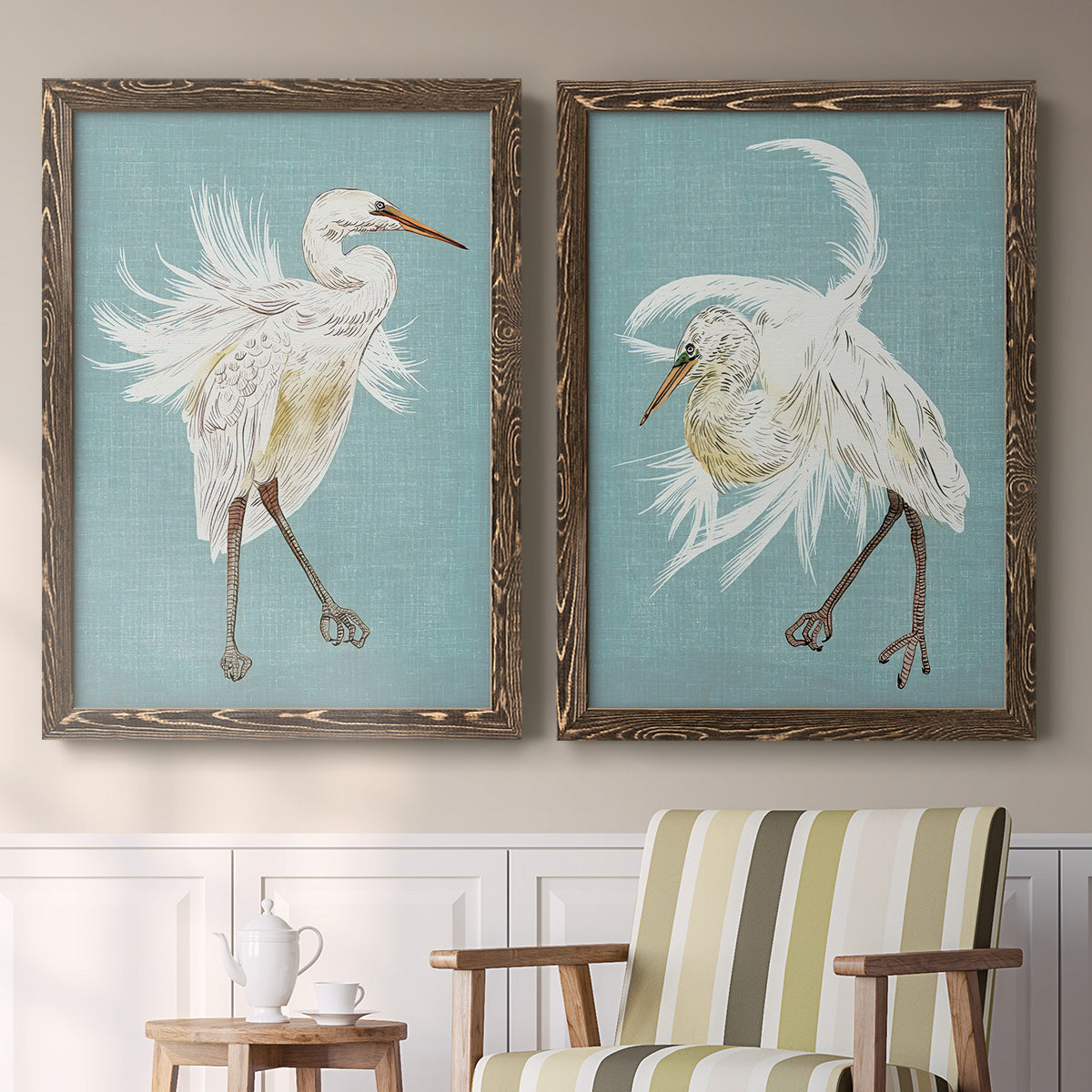 Set of two walnut barnwood framed canvas prints depicting two decorative bird illustrations featuring white herons displaying long windswept feathers above a sideboard in a cozy sitting room.