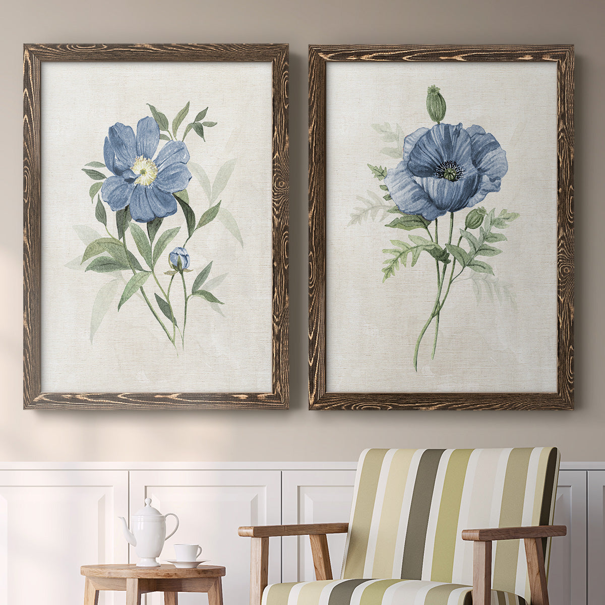 Set of two walnut barnwood framed canvas prints depicting two farmhouse botanical illustrations featuring blue periwinkle flowers with leafy stems above a sideboard in a cozy sitting room.