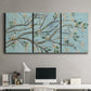 Three-panel canvas wall art featuring blue sky with flowering branches, displayed above a desk in a home office.