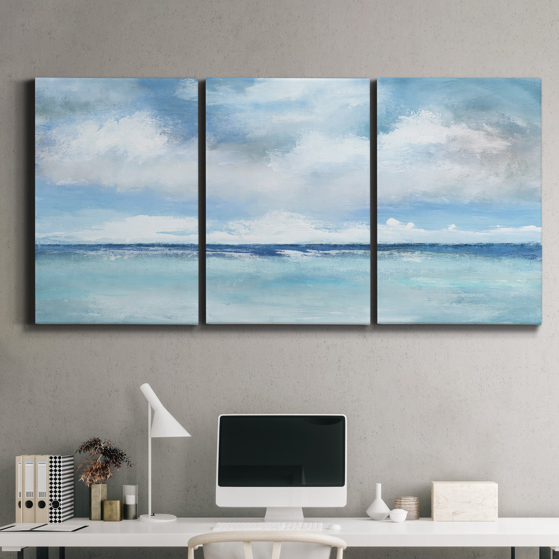 Three-panel canvas wall art featuring tropical clouds over ocean horizon, displayed above a desk in a home office.