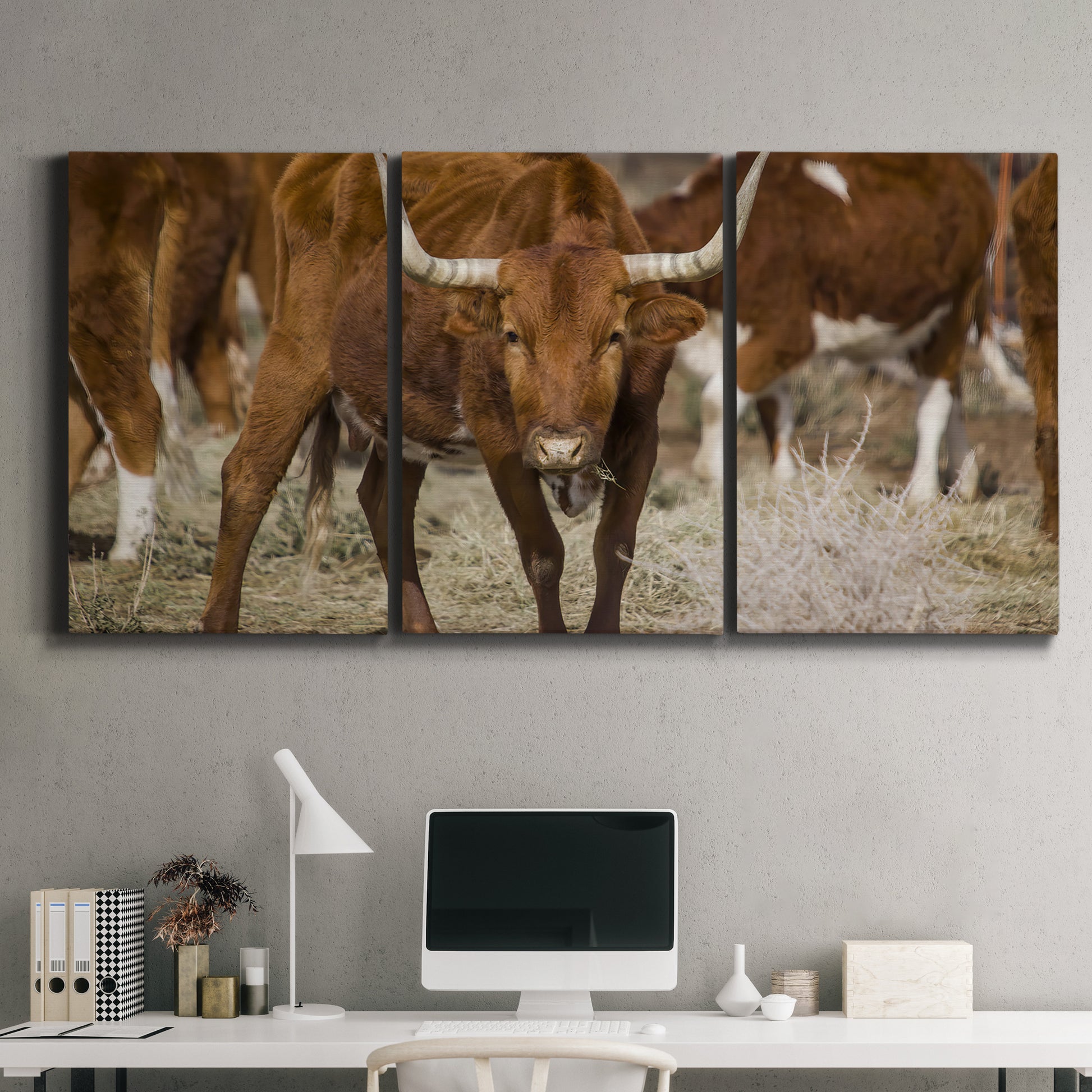 Three-panel canvas wall art featuring longhorn cattle standing together, displayed above a desk in a home office.
