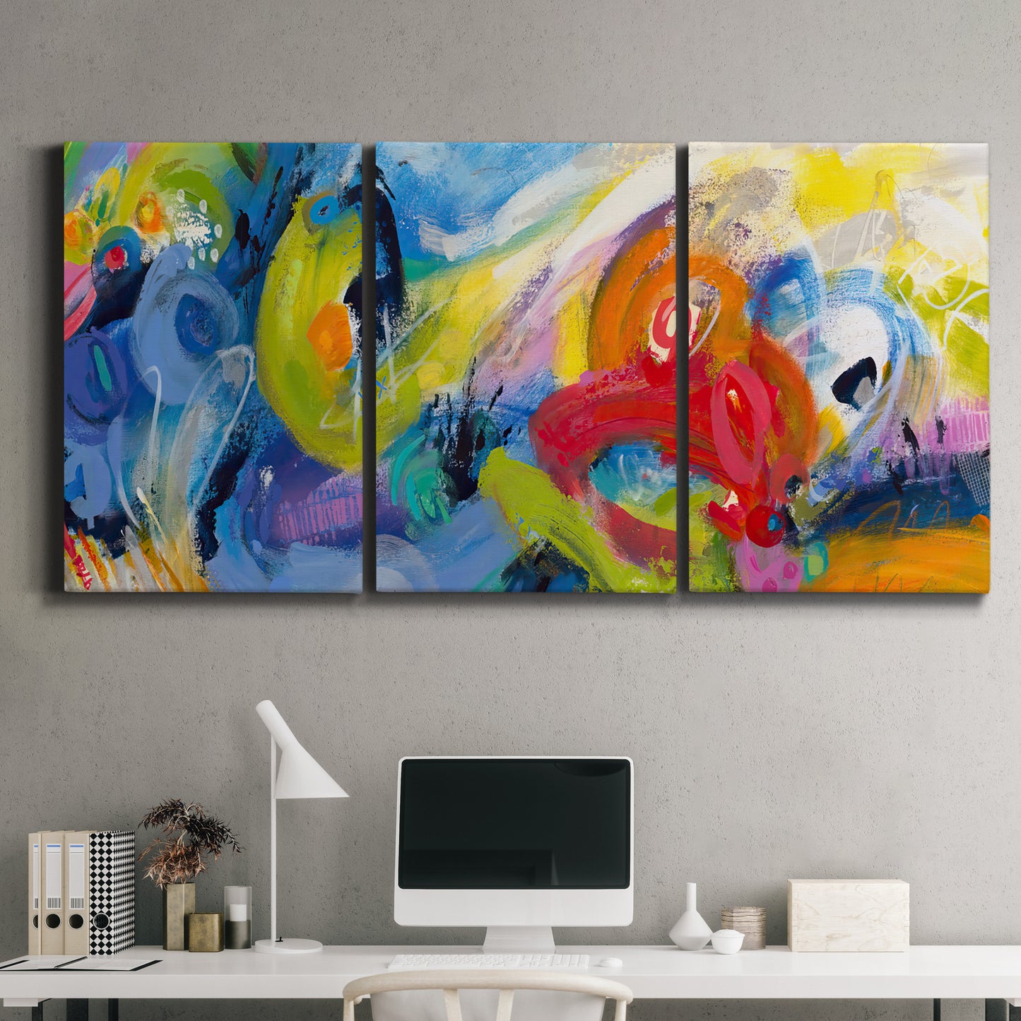 Three-panel canvas wall art featuring colorful abstract racing forms, displayed above a desk in a home office.