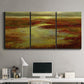 Three-panel canvas wall art featuring coastal shoreline with warm light, displayed above a desk in a home office.