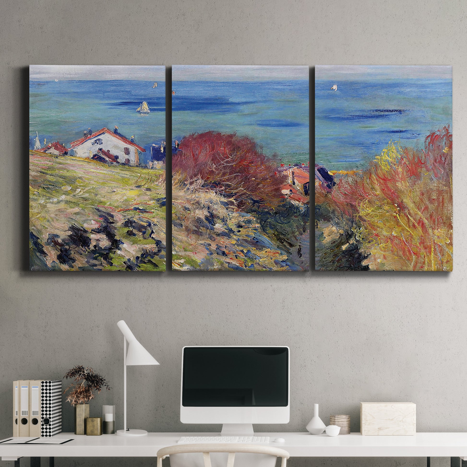 Three-panel canvas wall art featuring coastal village shoreline landscape, displayed above a desk in a home office.