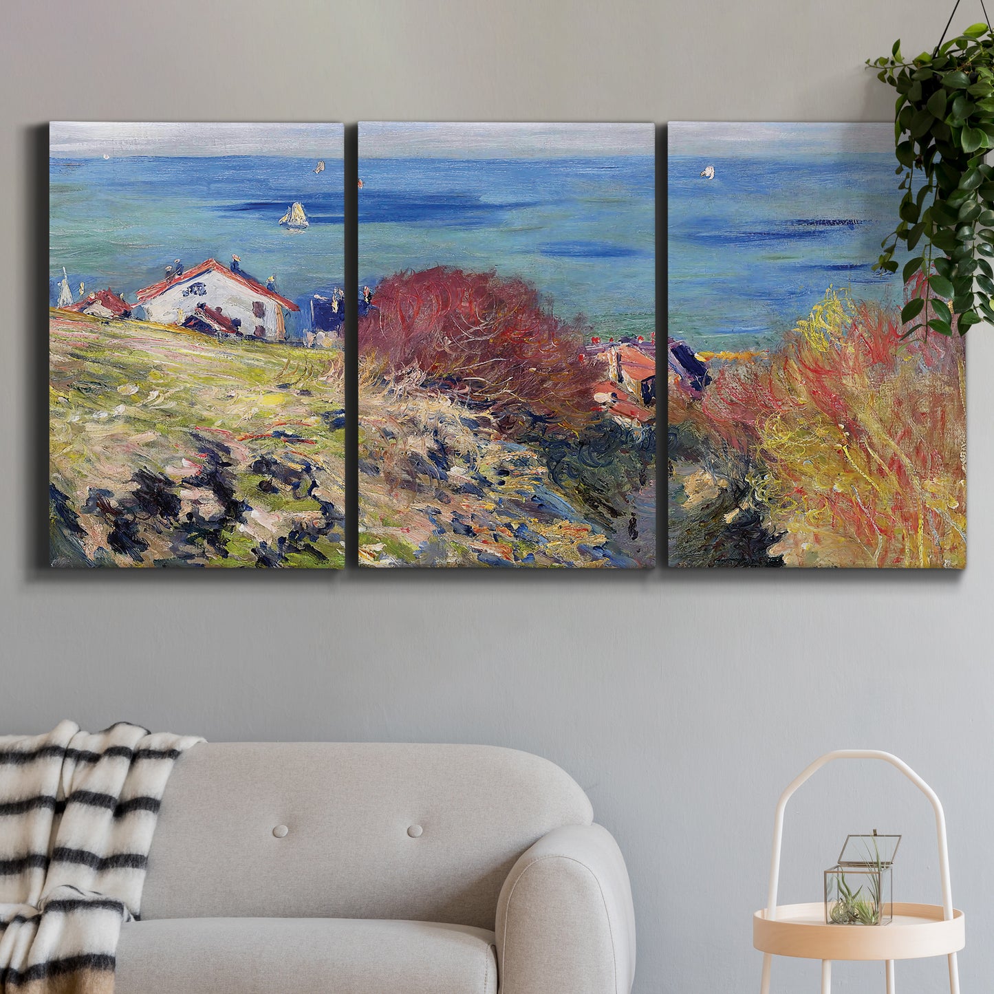 Three-panel canvas wall art featuring coastal village shoreline landscape, displayed in a modern living room above a sofa.