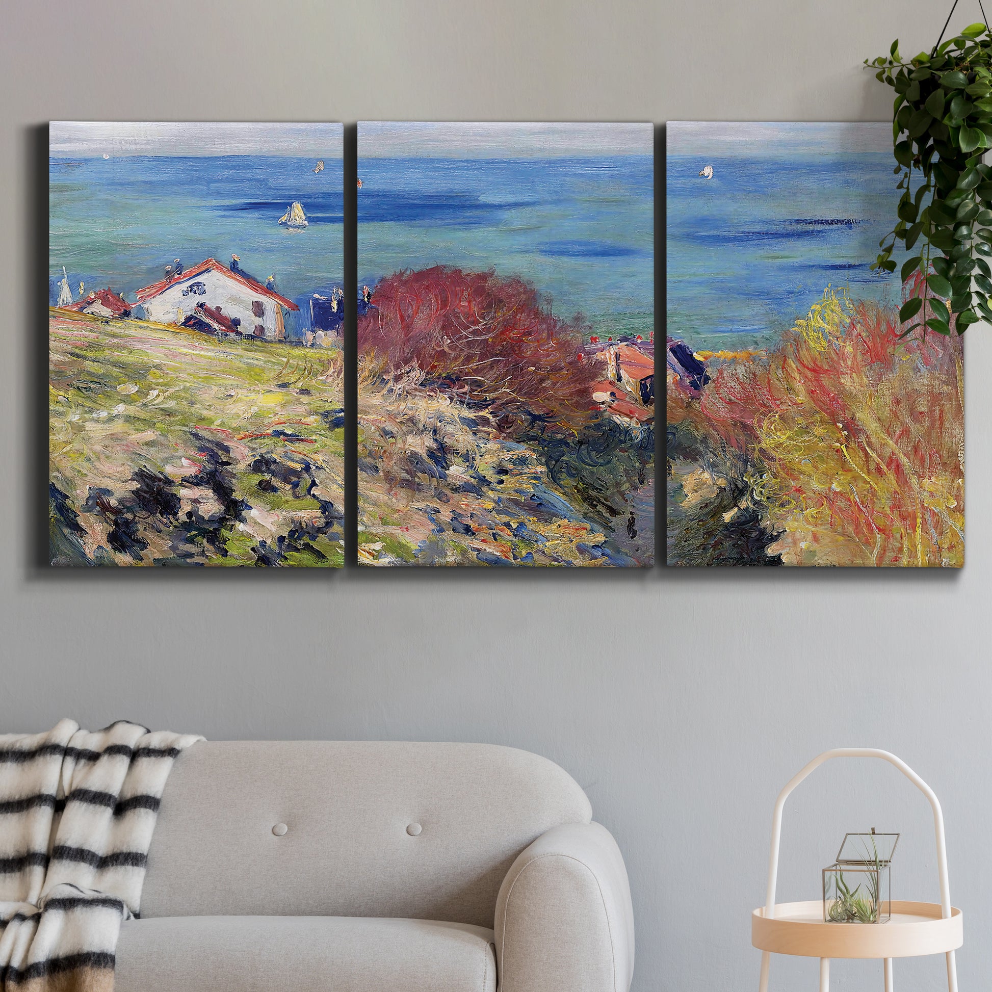 Three-panel canvas wall art featuring coastal village shoreline landscape, displayed in a modern living room above a sofa.