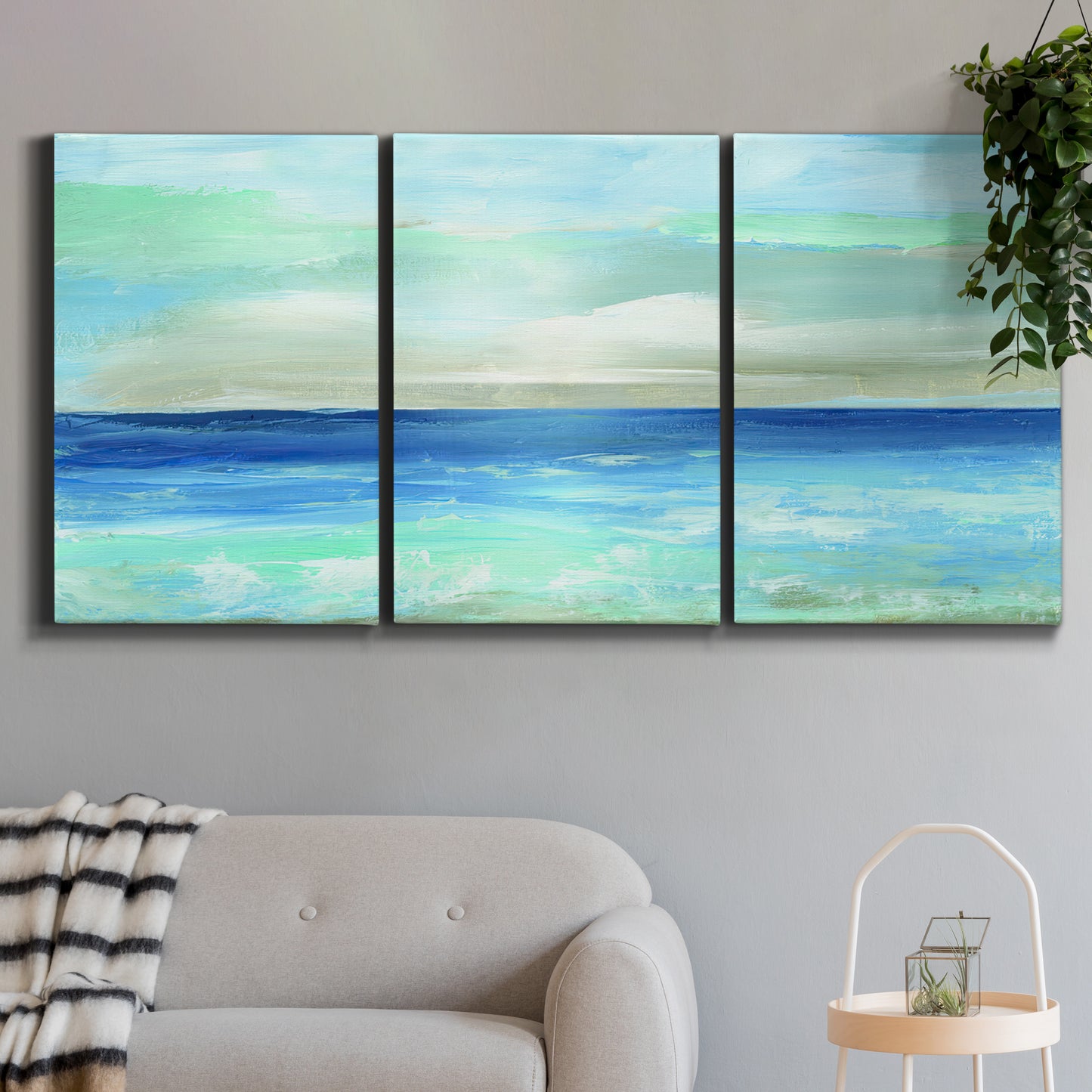 Three-panel canvas wall art featuring vast open blue ocean horizon, displayed in a modern living room above a sofa.