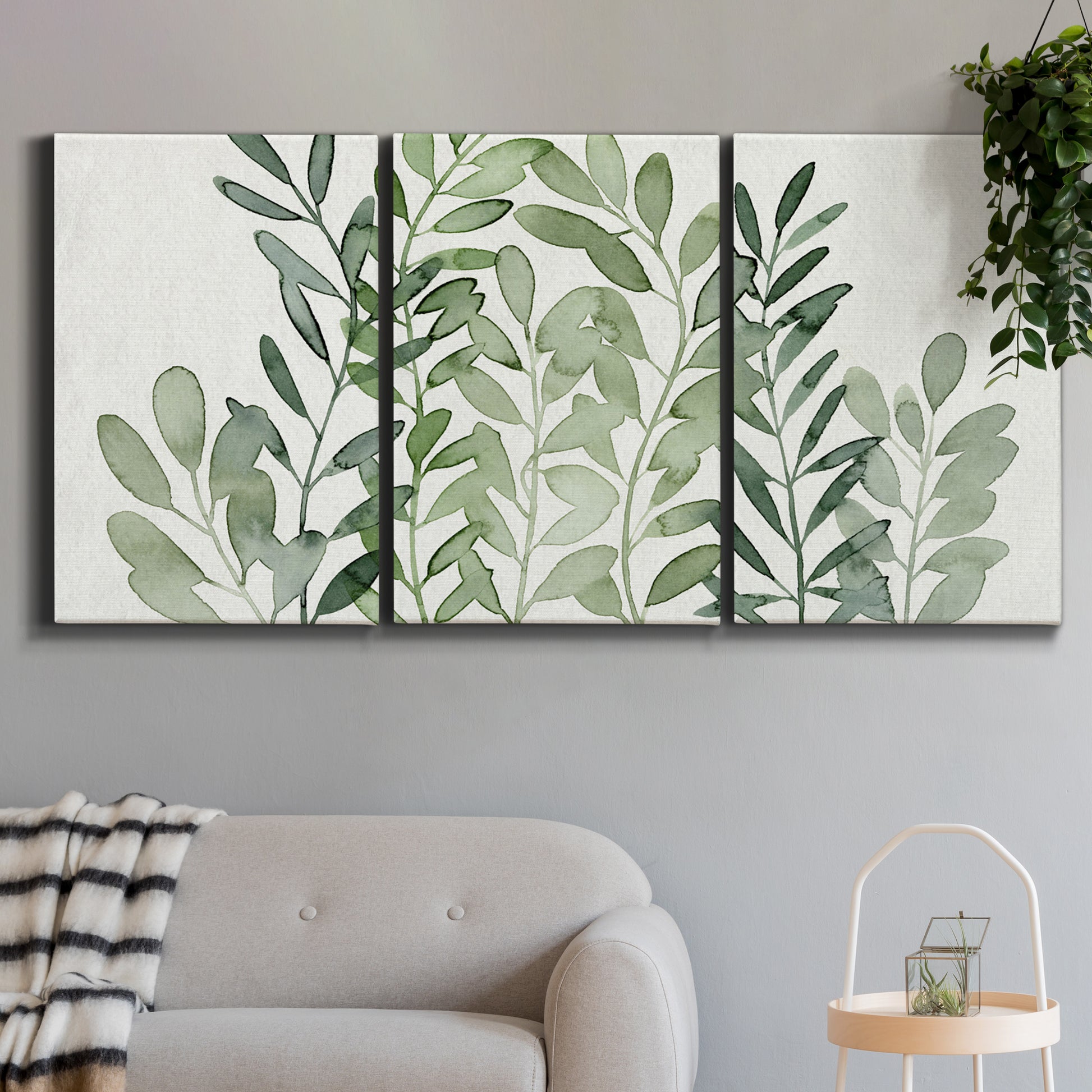 Three-panel canvas wall art featuring foraged leafy greens botanical study, displayed in a modern living room above a sofa.