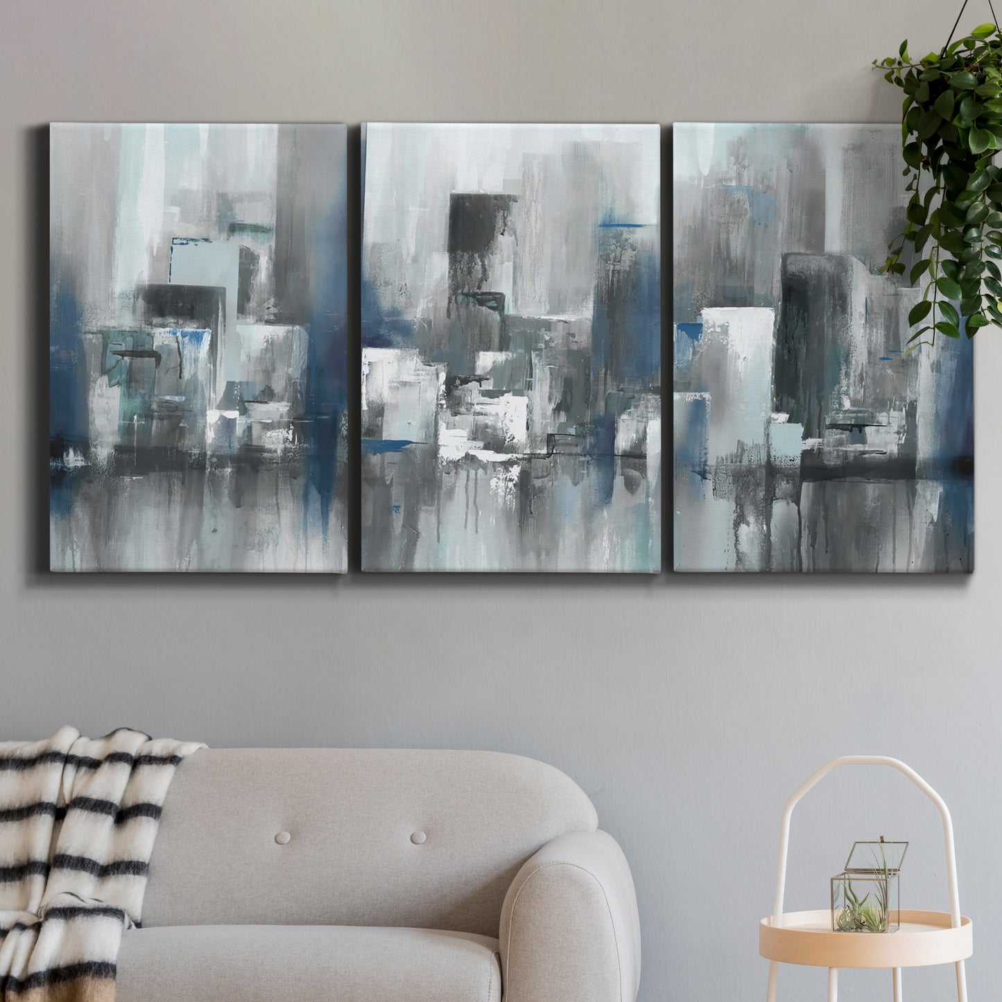 Three-panel canvas wall art featuring urban cityscape rendered in blue tones, displayed in a modern living room above a sofa.