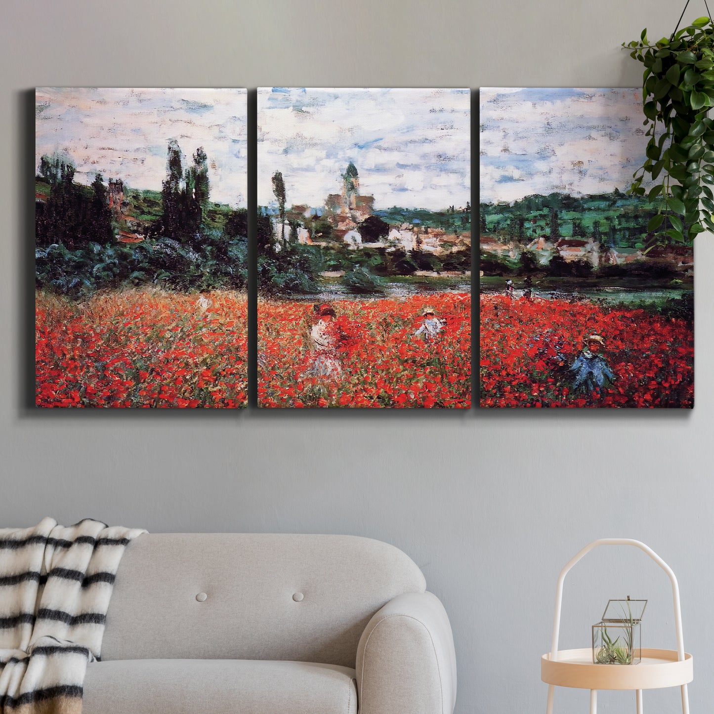 Three-panel canvas wall art featuring poppy field beside village landscape, displayed in a modern living room above a sofa.