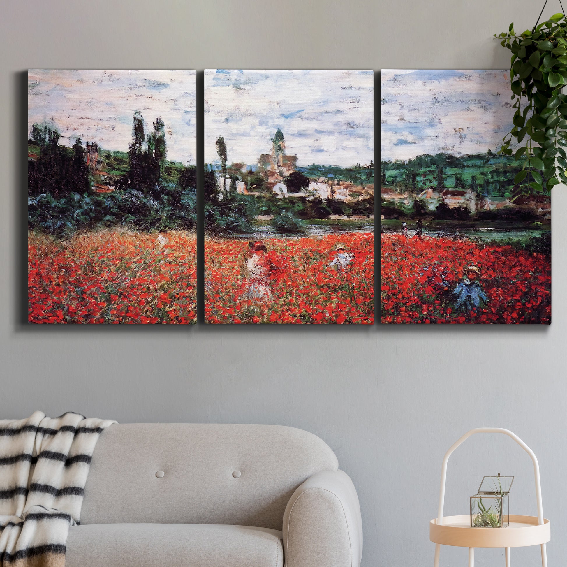 Three-panel canvas wall art featuring poppy field beside village landscape, displayed in a modern living room above a sofa.