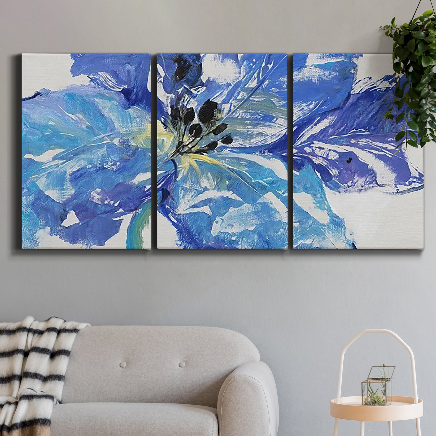 Three-panel canvas wall art featuring blue floral botanical close up, displayed in a modern living room above a sofa.