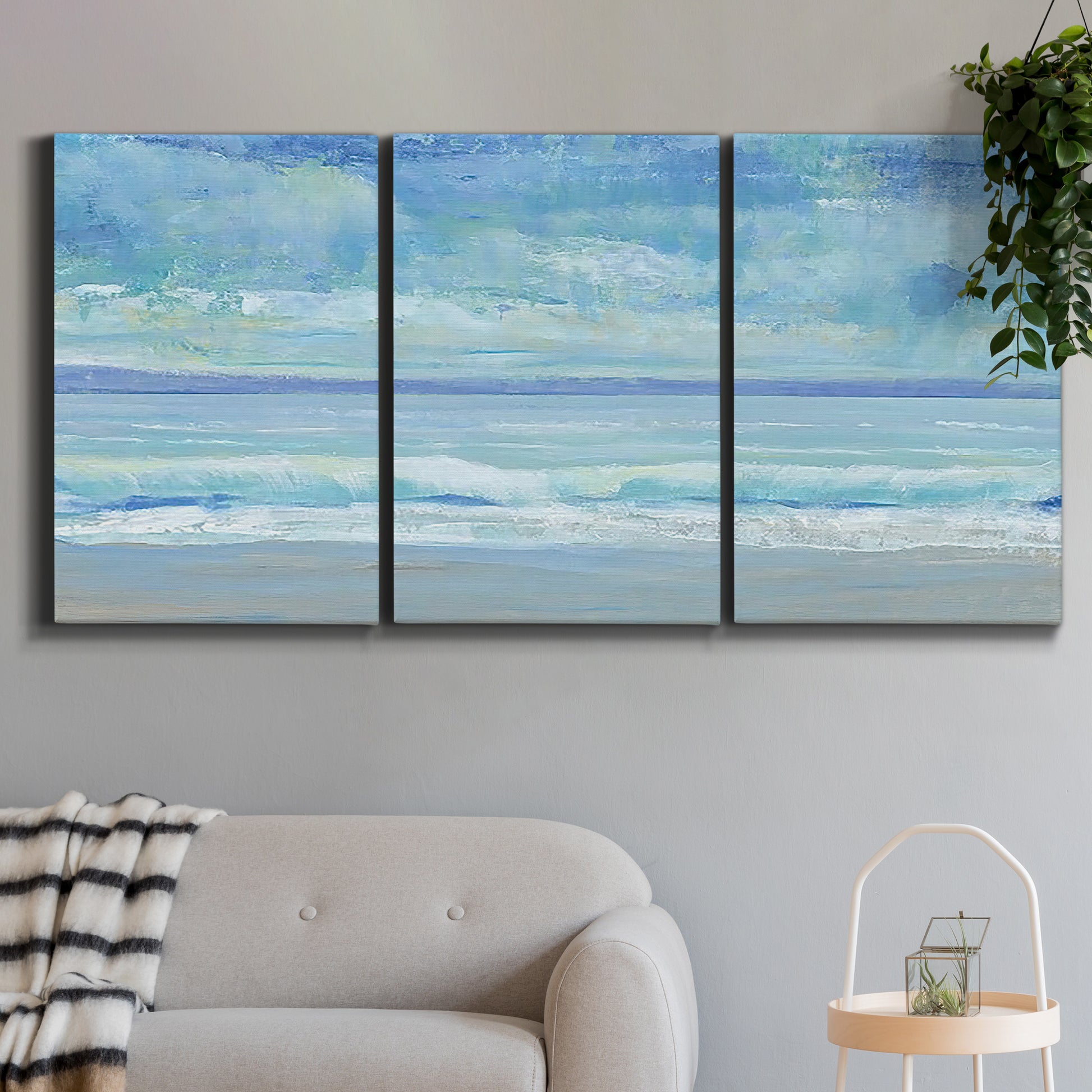 Three-panel canvas wall art featuring rolling ocean surf along shoreline, displayed in a modern living room above a sofa.
