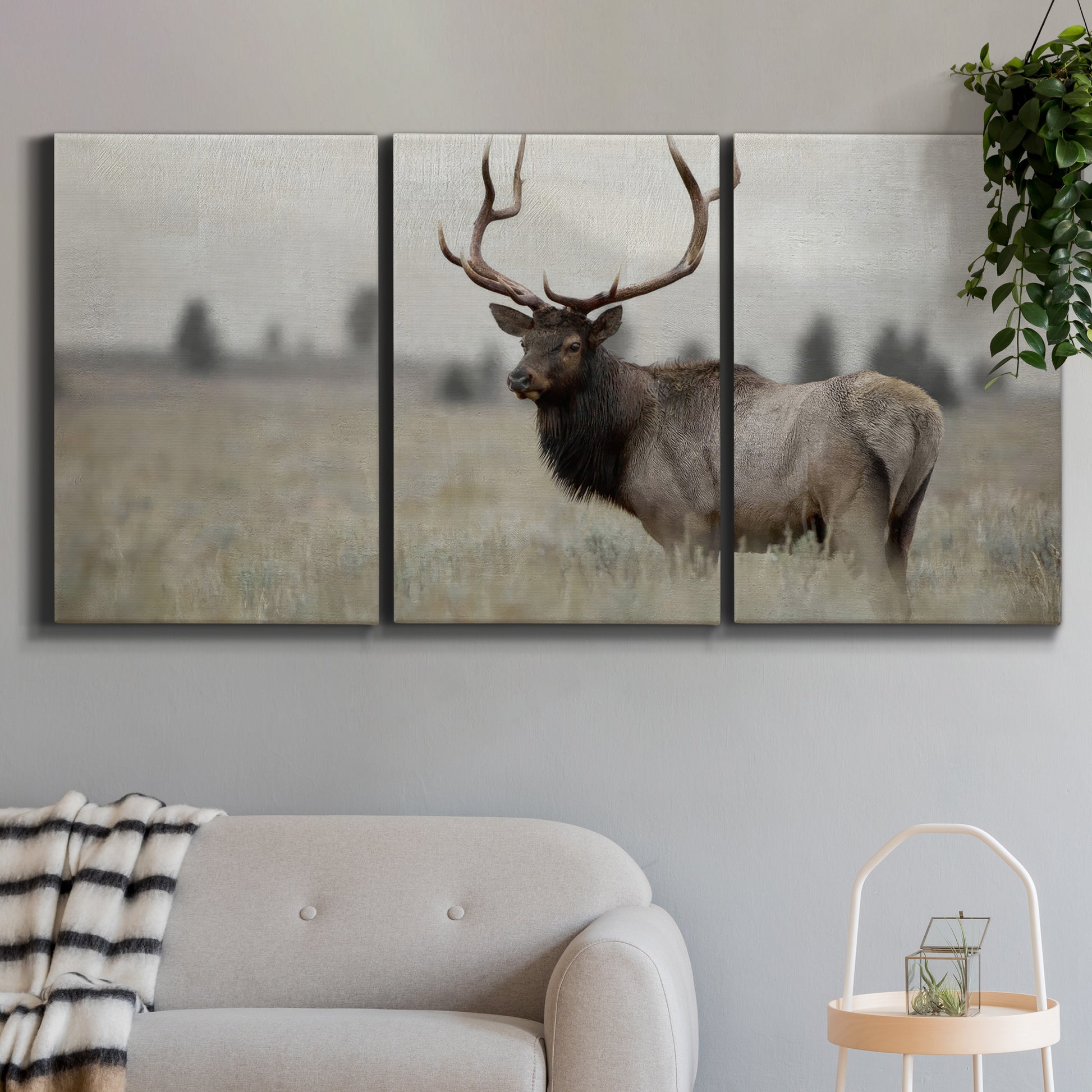 Three-panel canvas wall art featuring elk standing in open grassland, displayed in a modern living room above a sofa.