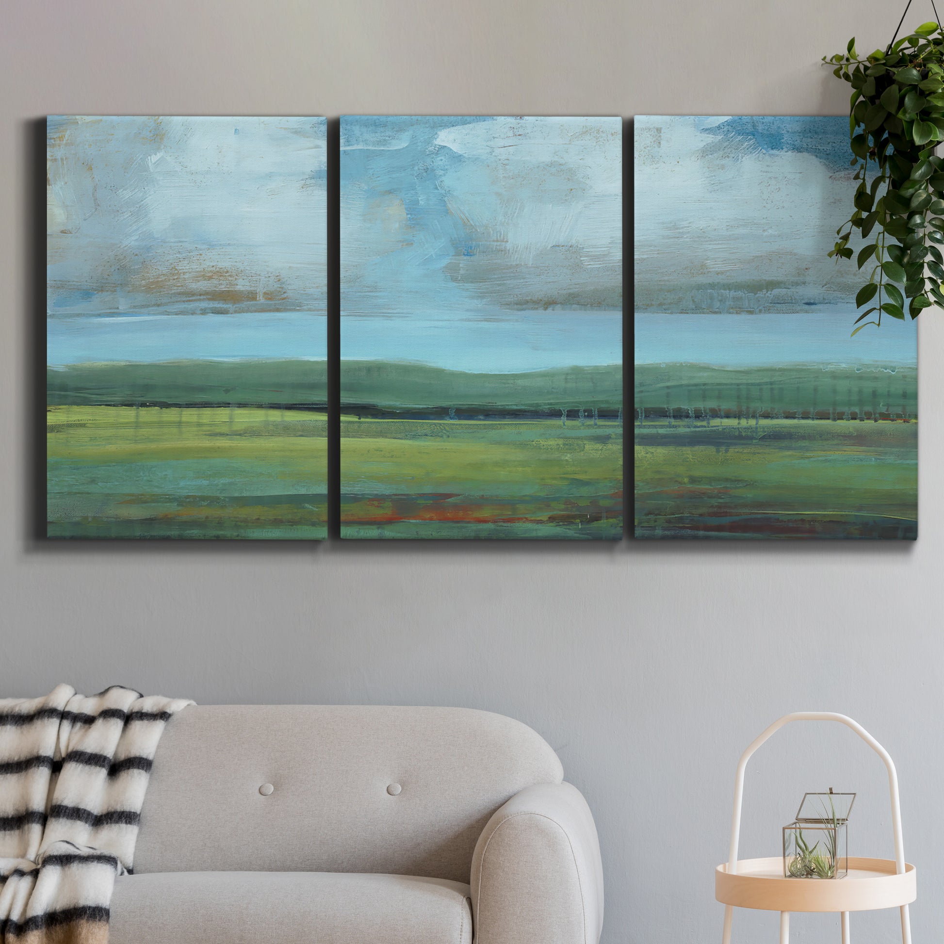 Three-panel canvas wall art featuring wide valley landscape with rolling hills, displayed in a modern living room above a sofa.