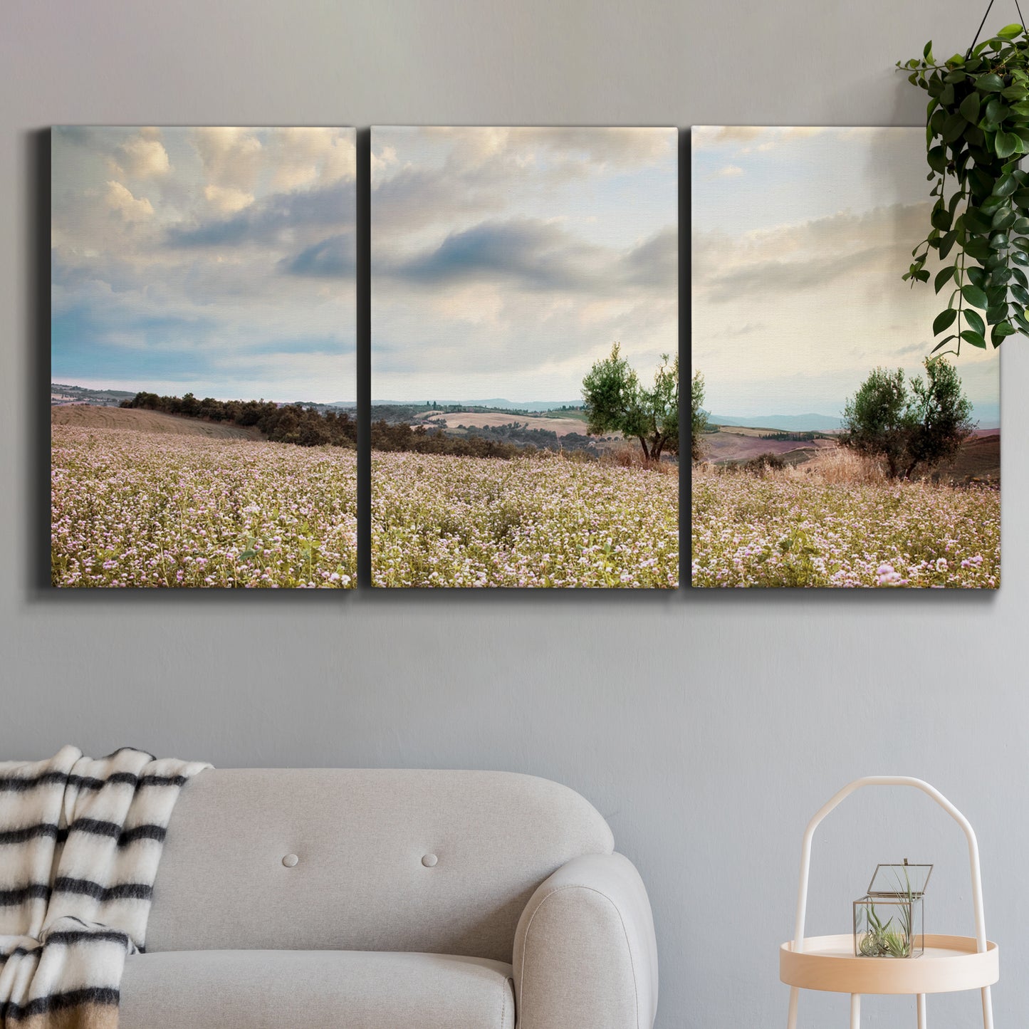 Three-panel canvas wall art featuring wildflowers across tuscan landscape, displayed in a modern living room above a sofa.
