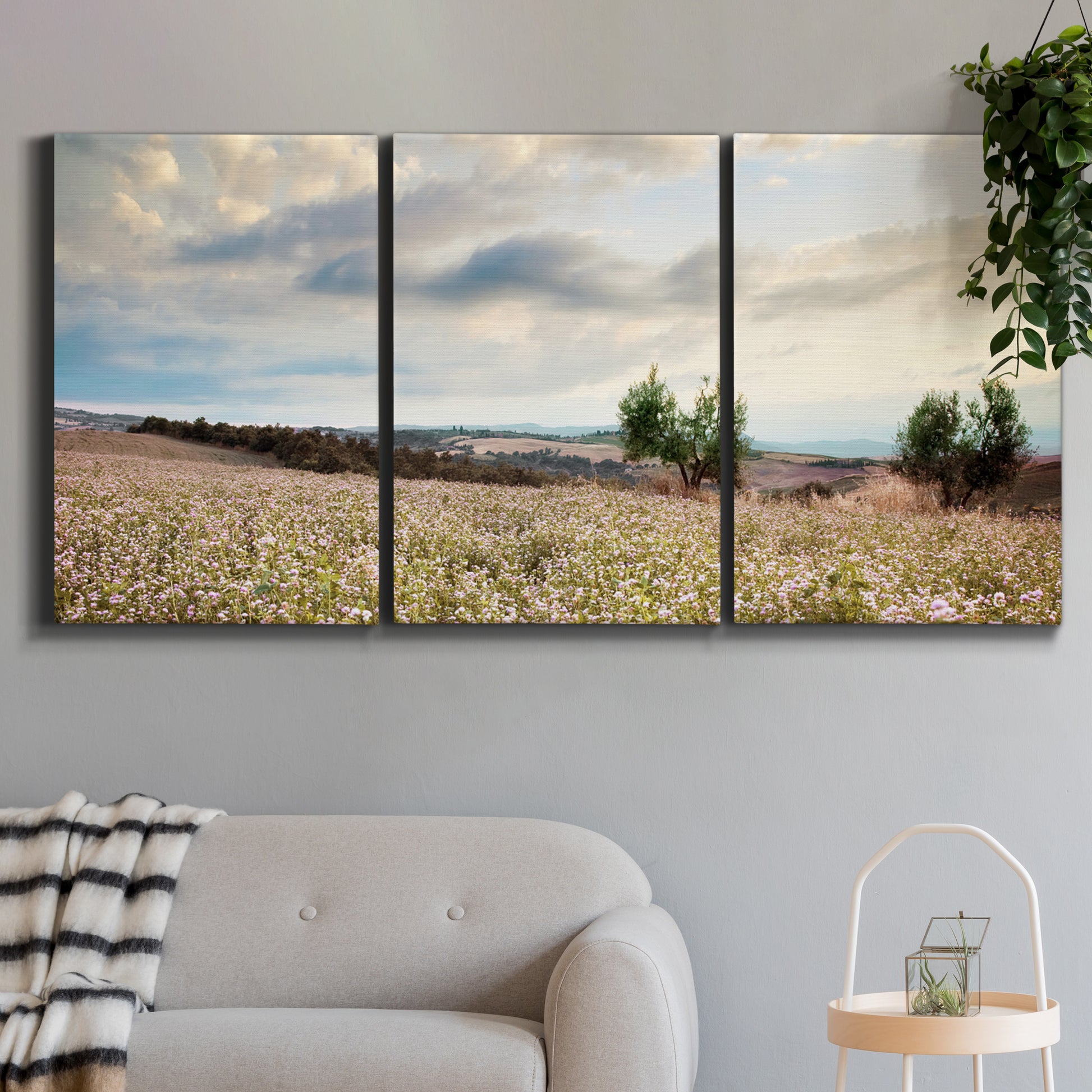 Three-panel canvas wall art featuring wildflowers across tuscan landscape, displayed in a modern living room above a sofa.