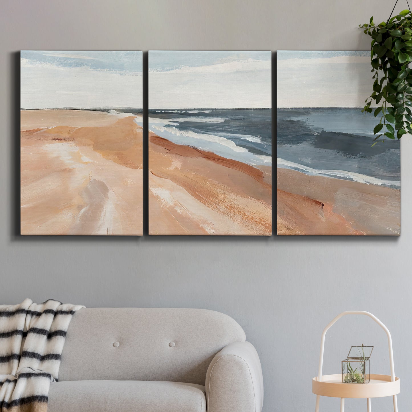 Three-panel canvas wall art featuring abstract coastal beach composition, displayed in a modern living room above a sofa.