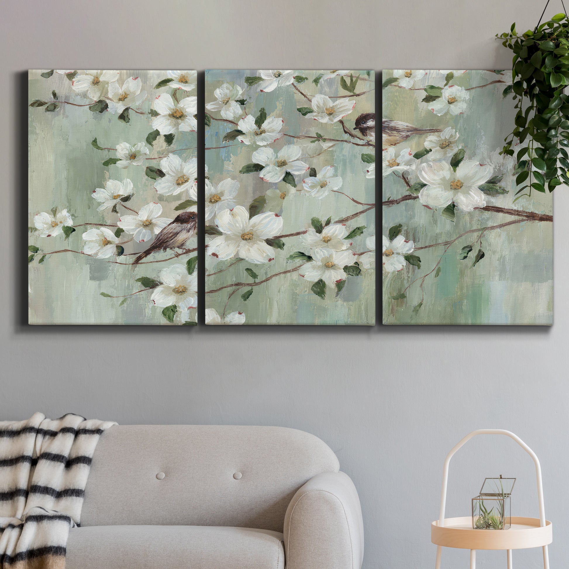 Three-panel canvas wall art featuring delicate spring blossoms with birds, displayed in a modern living room above a sofa.