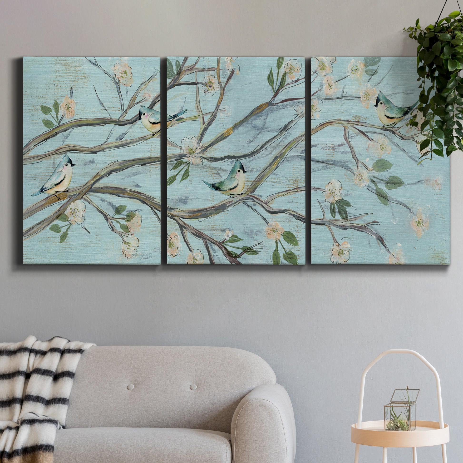 Three-panel canvas wall art featuring blue sky with flowering branches, displayed in a modern living room above a sofa.