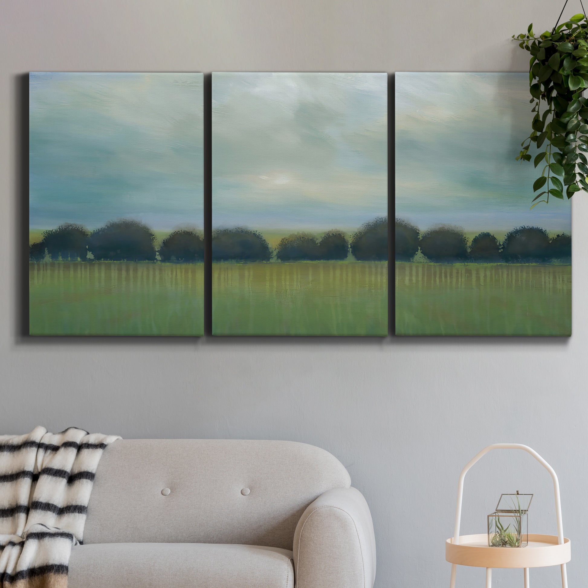 Three-panel canvas wall art featuring rolling green pastoral fields, displayed in a modern living room above a sofa.