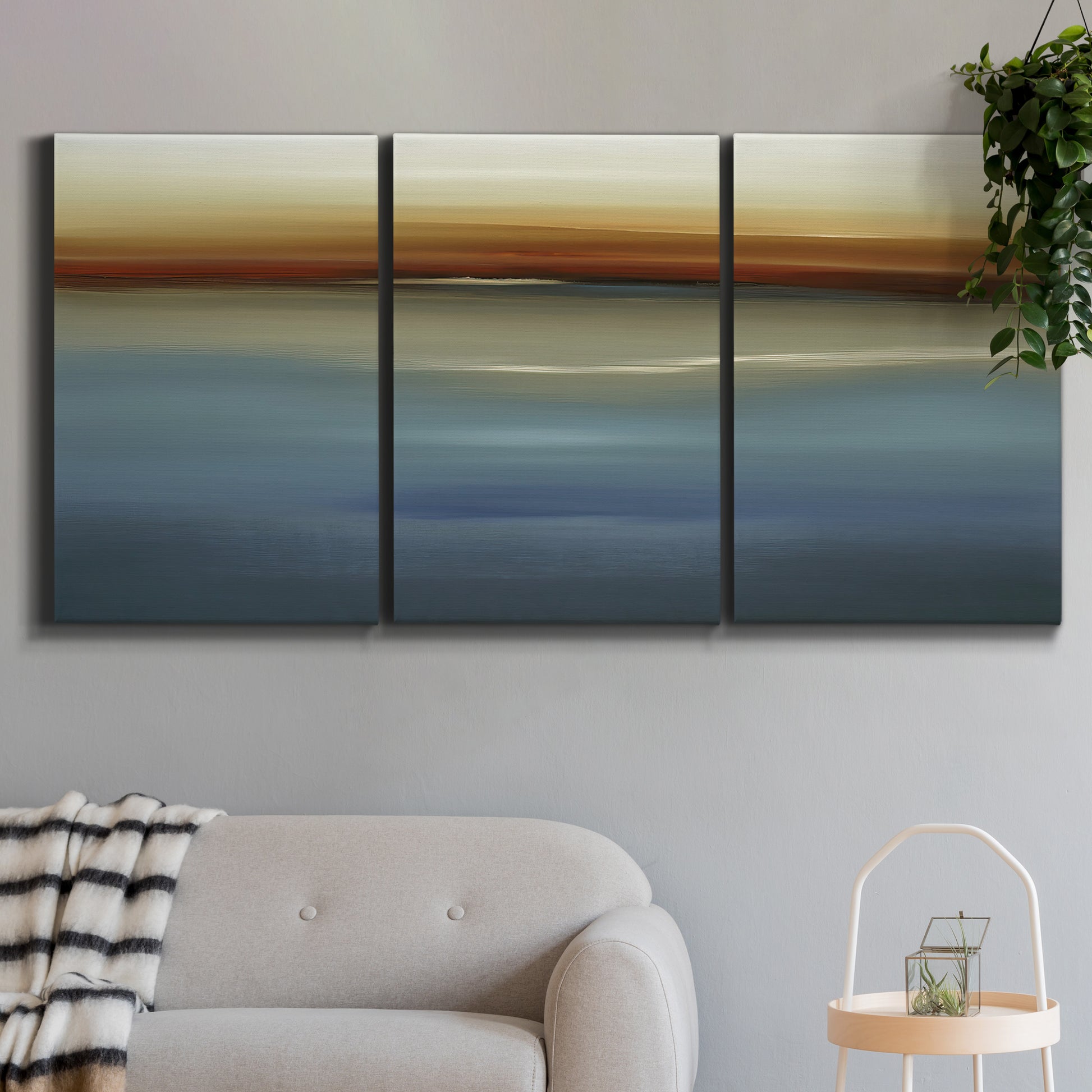 Three-panel canvas wall art featuring horizontal abstract coastal color bands, displayed in a modern living room above a sofa.