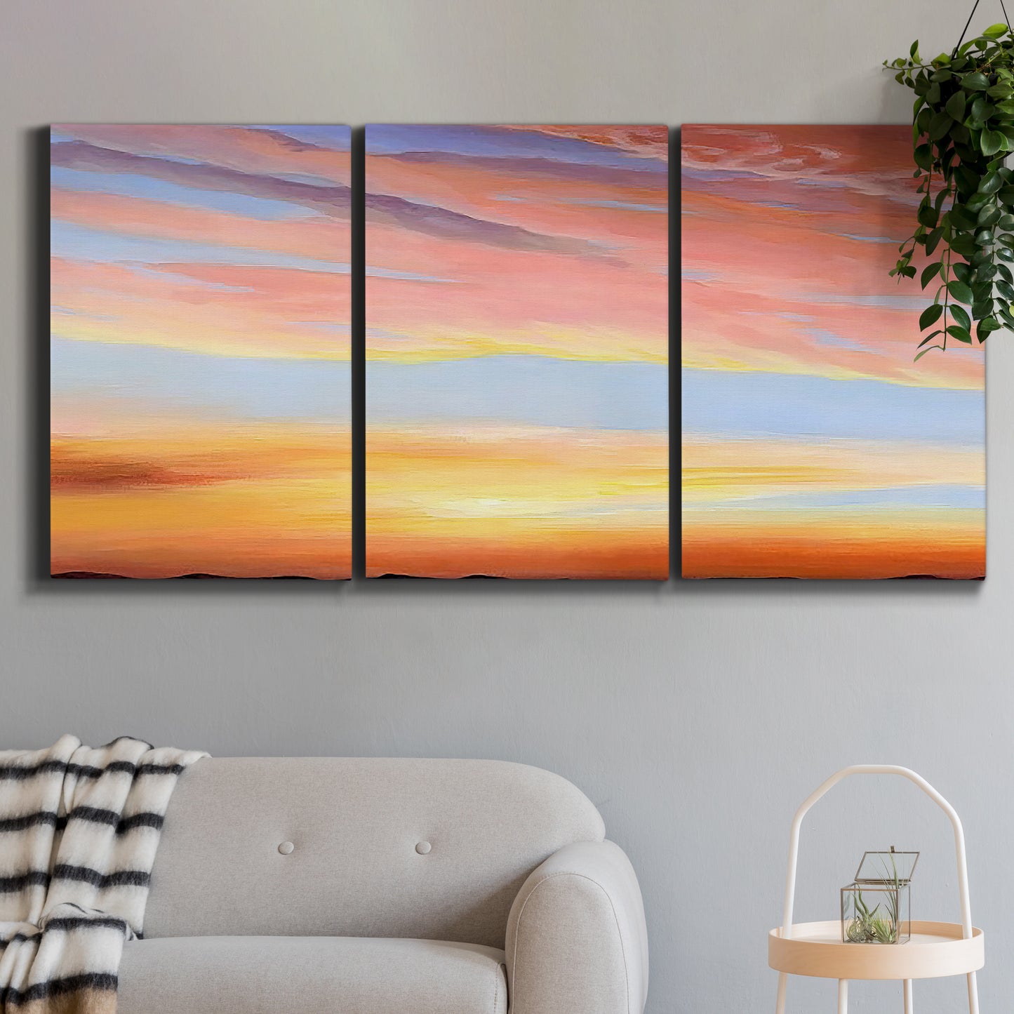 Three-panel canvas wall art featuring glowing sunset sky over landscape, displayed in a modern living room above a sofa.