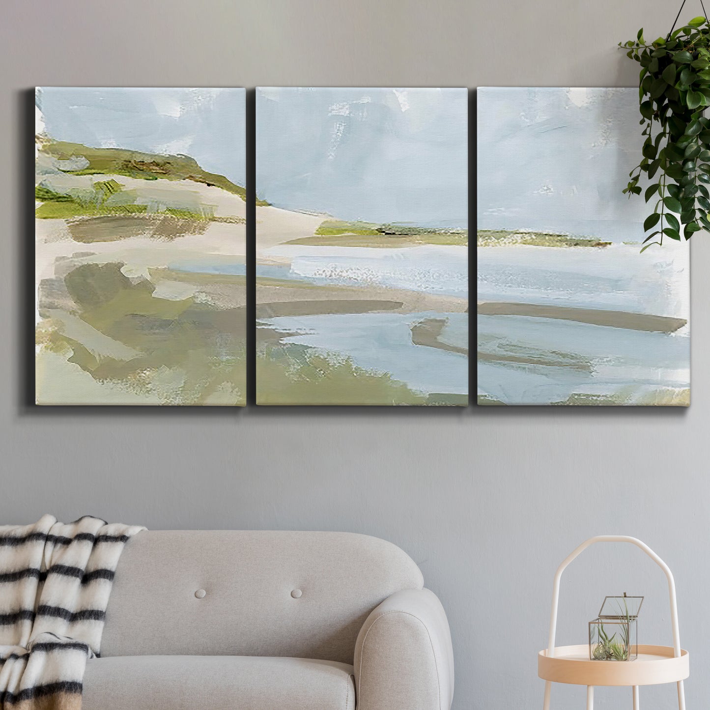 Three-panel canvas wall art featuring coastal cove with calm water, displayed in a modern living room above a sofa.