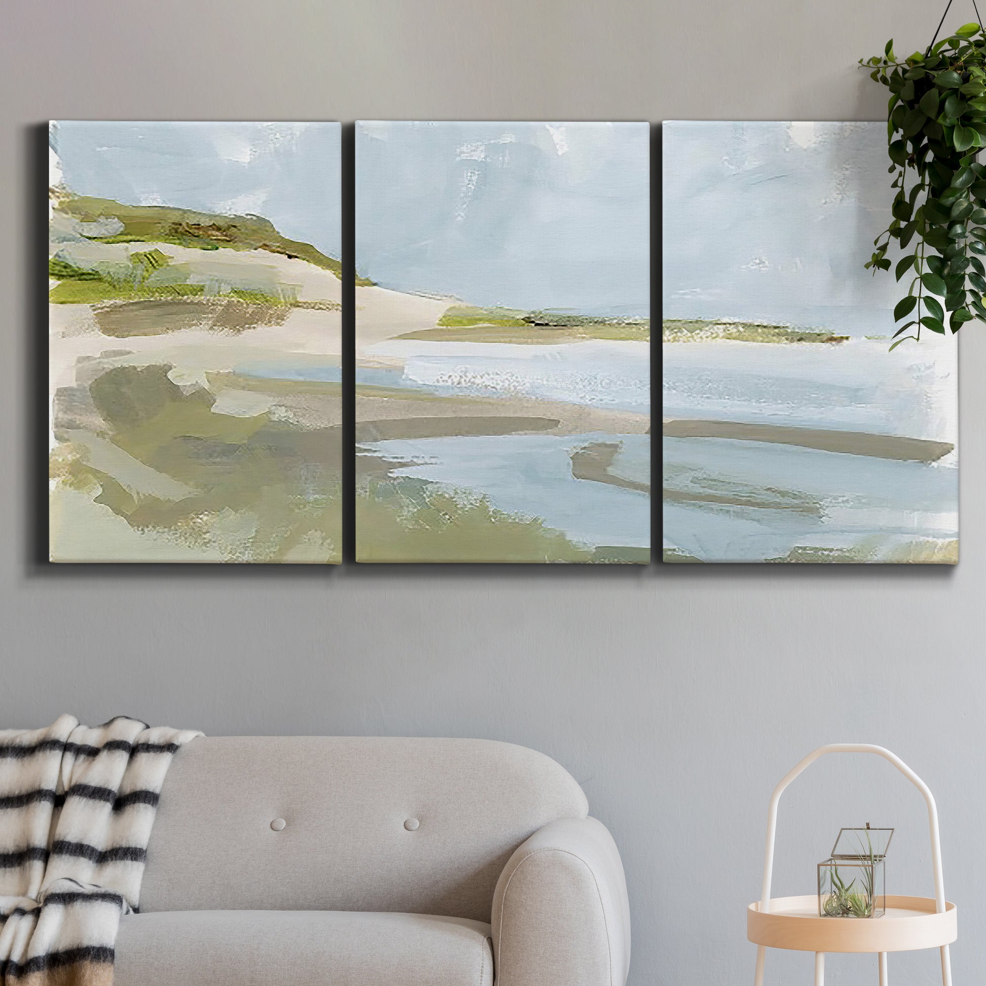 Three-panel canvas wall art featuring coastal cove with calm water, displayed in a modern living room above a sofa.