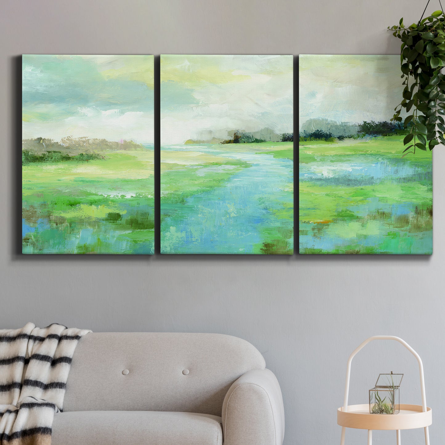 Three-panel canvas wall art featuring gentle stream winding through trees, displayed in a modern living room above a sofa.
