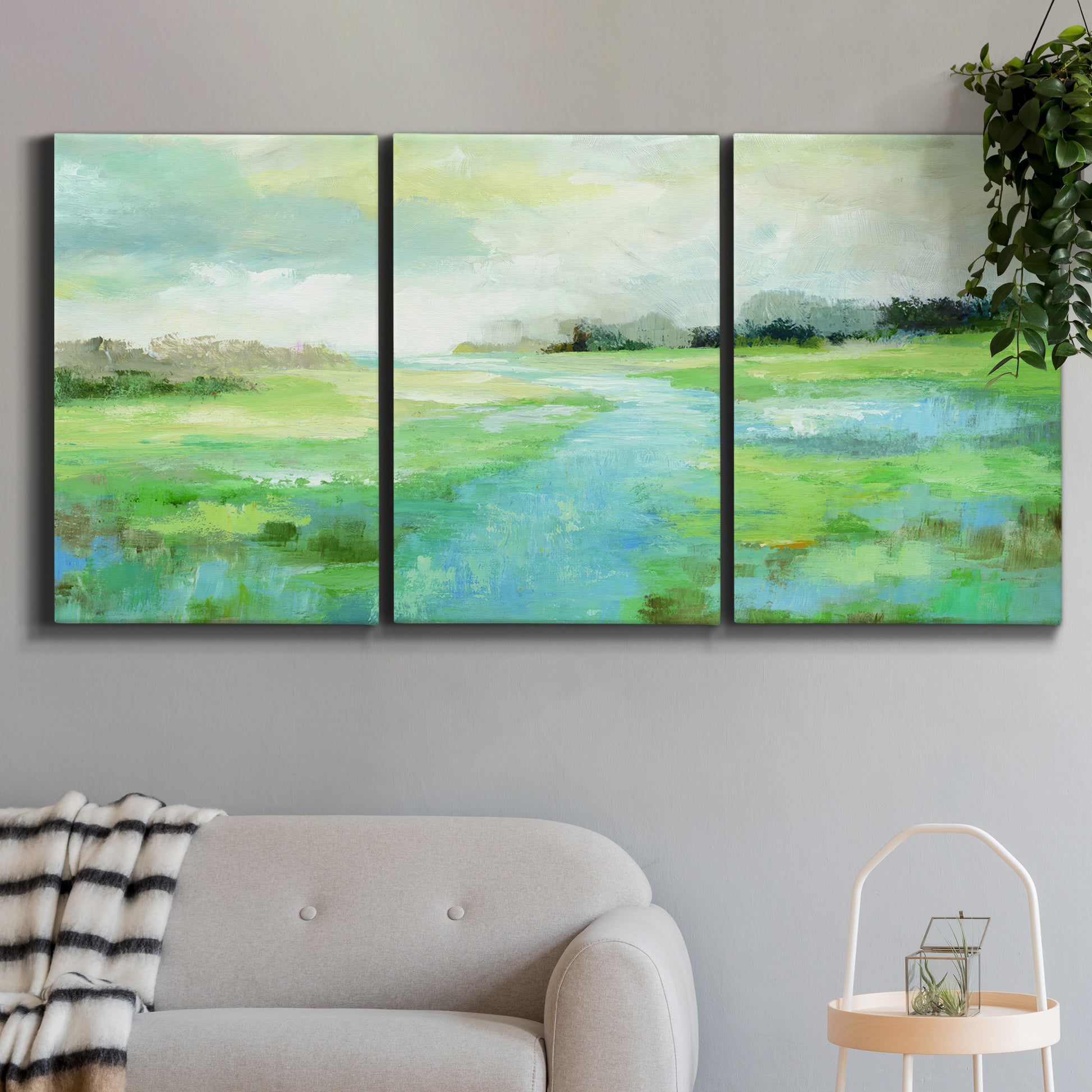 Three-panel canvas wall art featuring gentle stream winding through trees, displayed in a modern living room above a sofa.