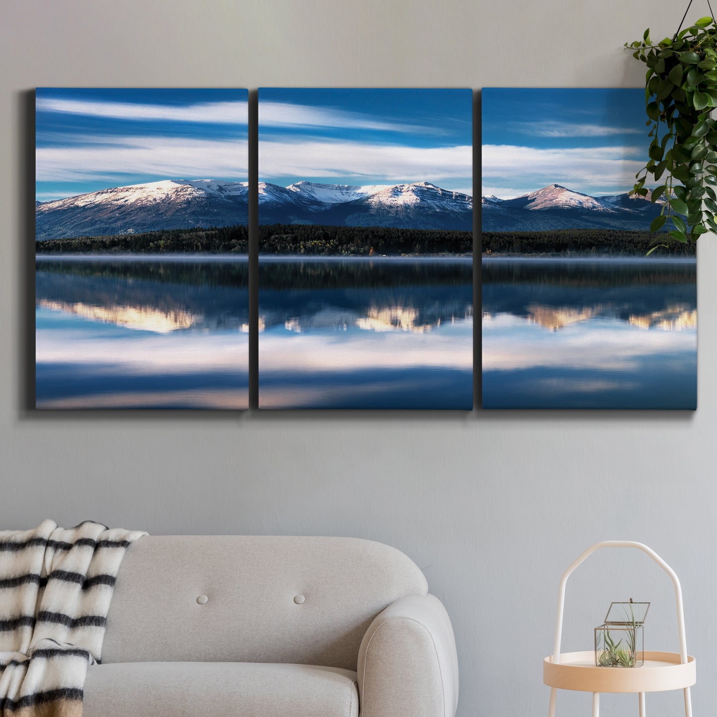 Three-panel canvas wall art featuring calm lake beneath mountains photograph, displayed in a modern living room above a sofa.